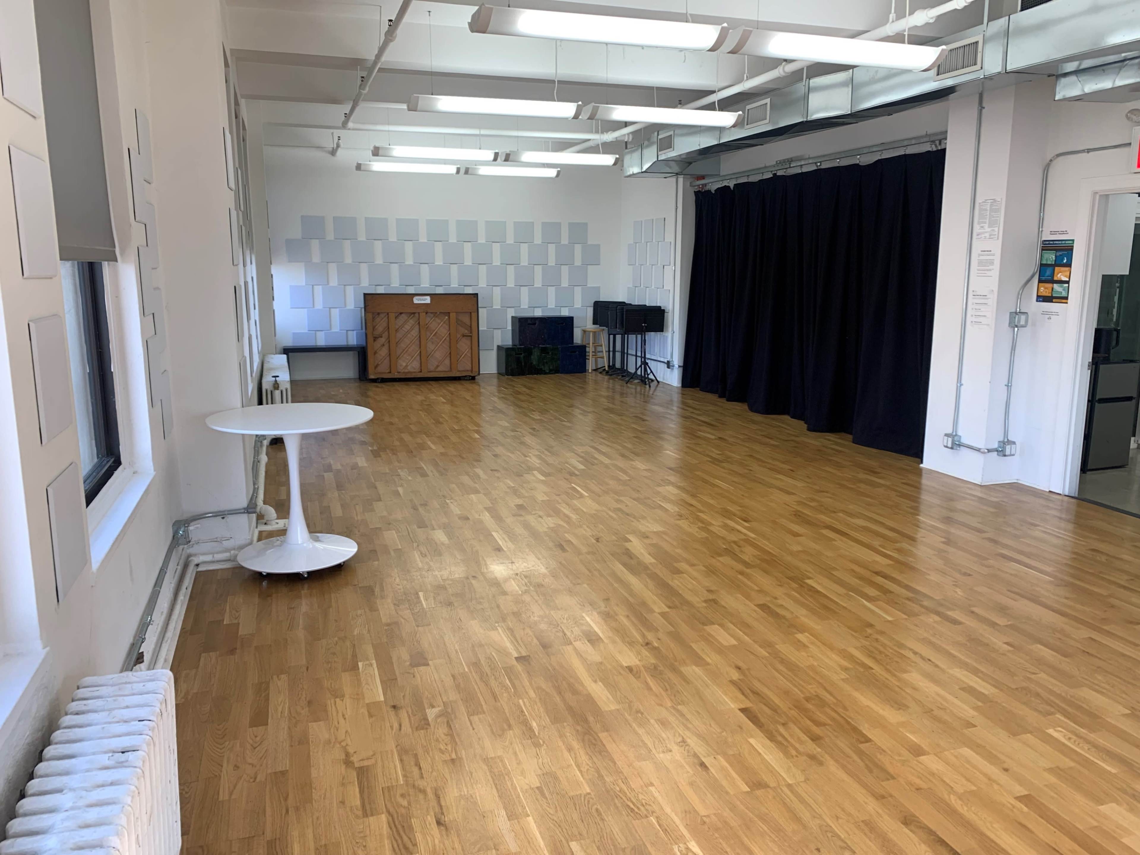 A spacious room with a wooden floor, a white circular table, a piano against the wall, and a black curtain in the background.