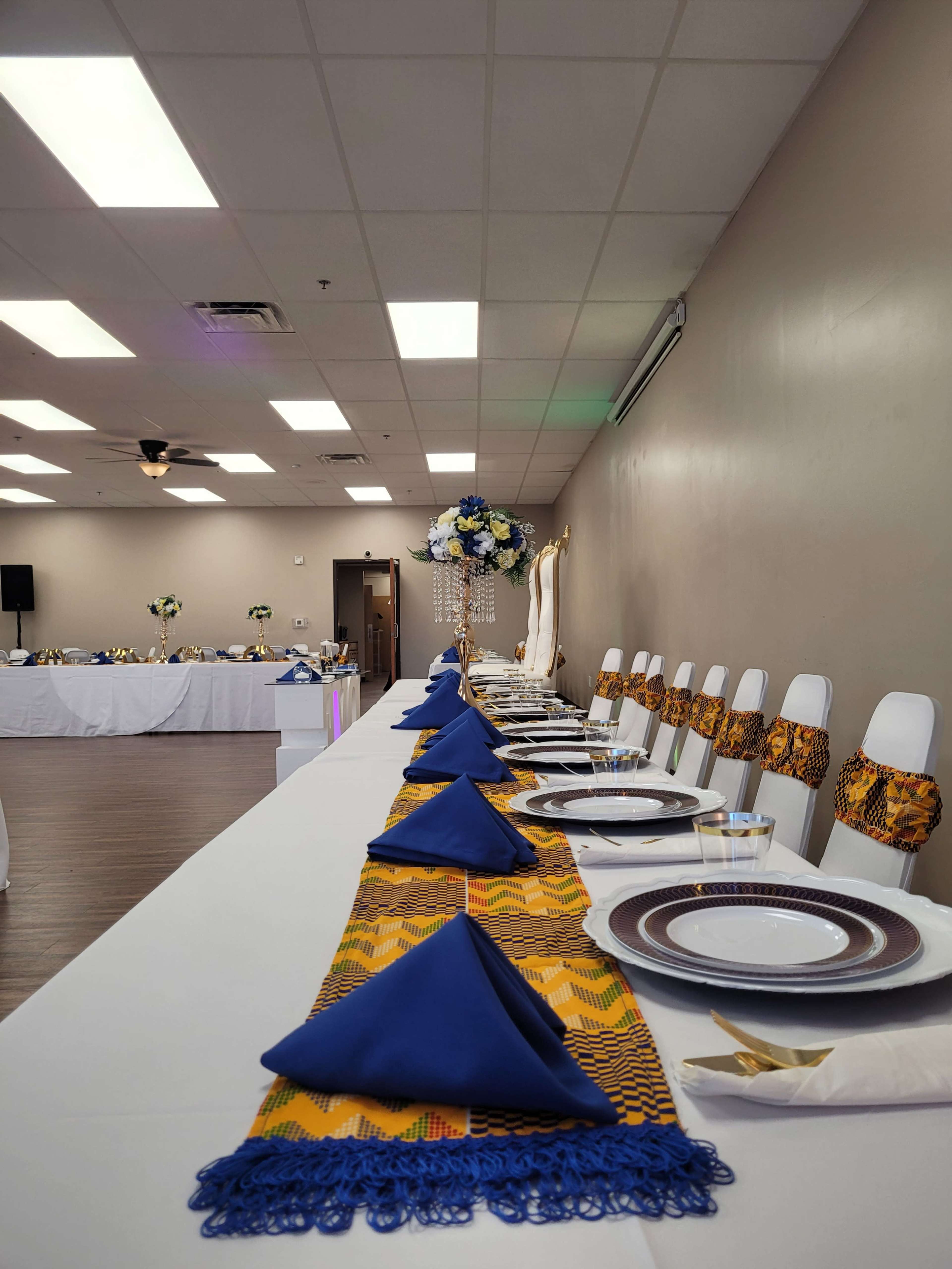 A long, elegantly set dining table is adorned with blue napkins and decorative centerpieces in a spacious event room.