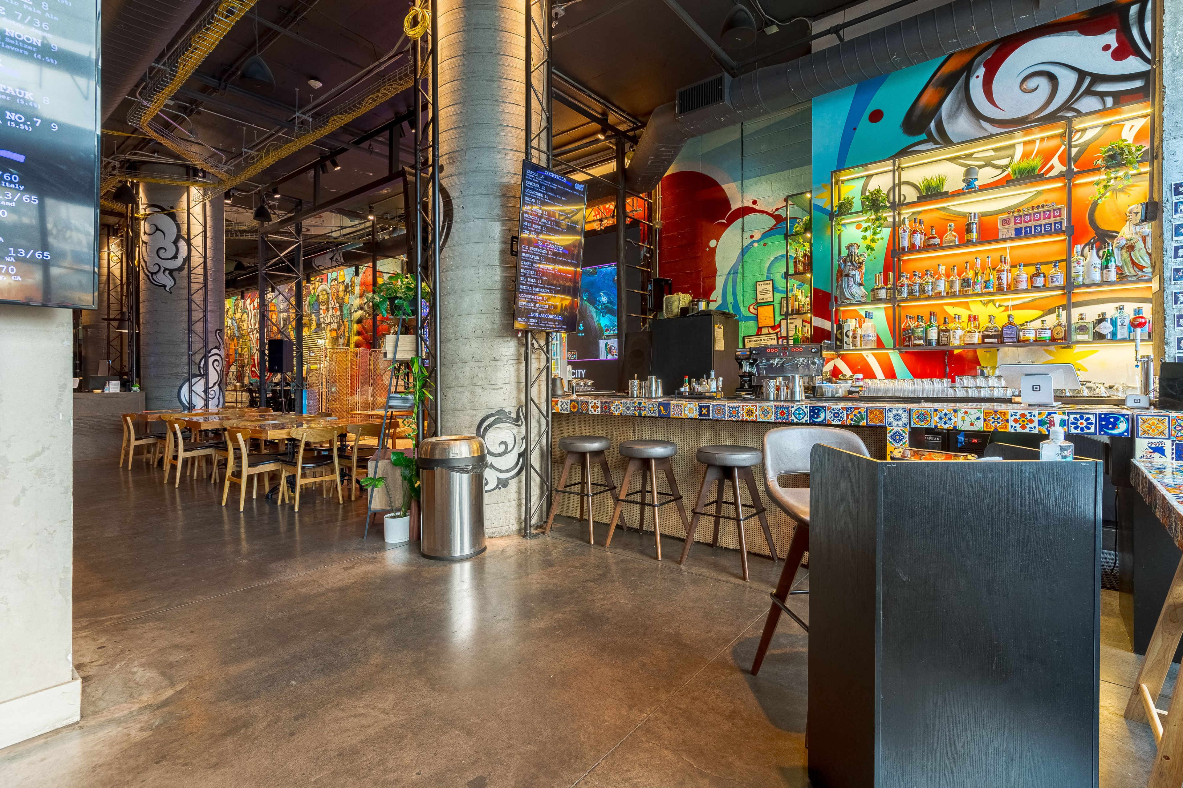 A vibrant restaurant interior featuring colorful murals, a bar area with illuminated shelves, and wooden dining tables arranged throughout the space.