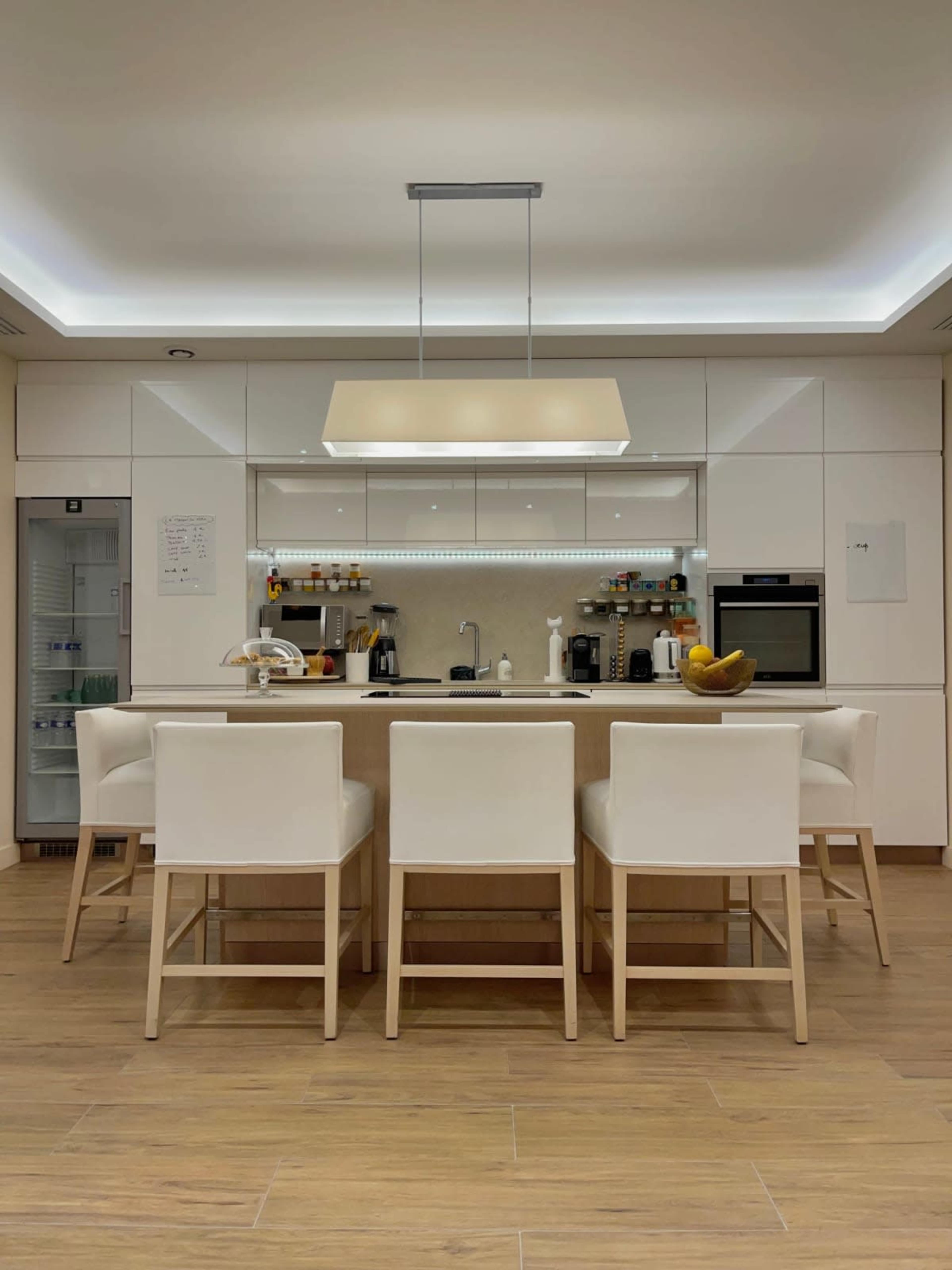 A modern kitchen with a central island, six white high-back stools, and sleek cabinetry.