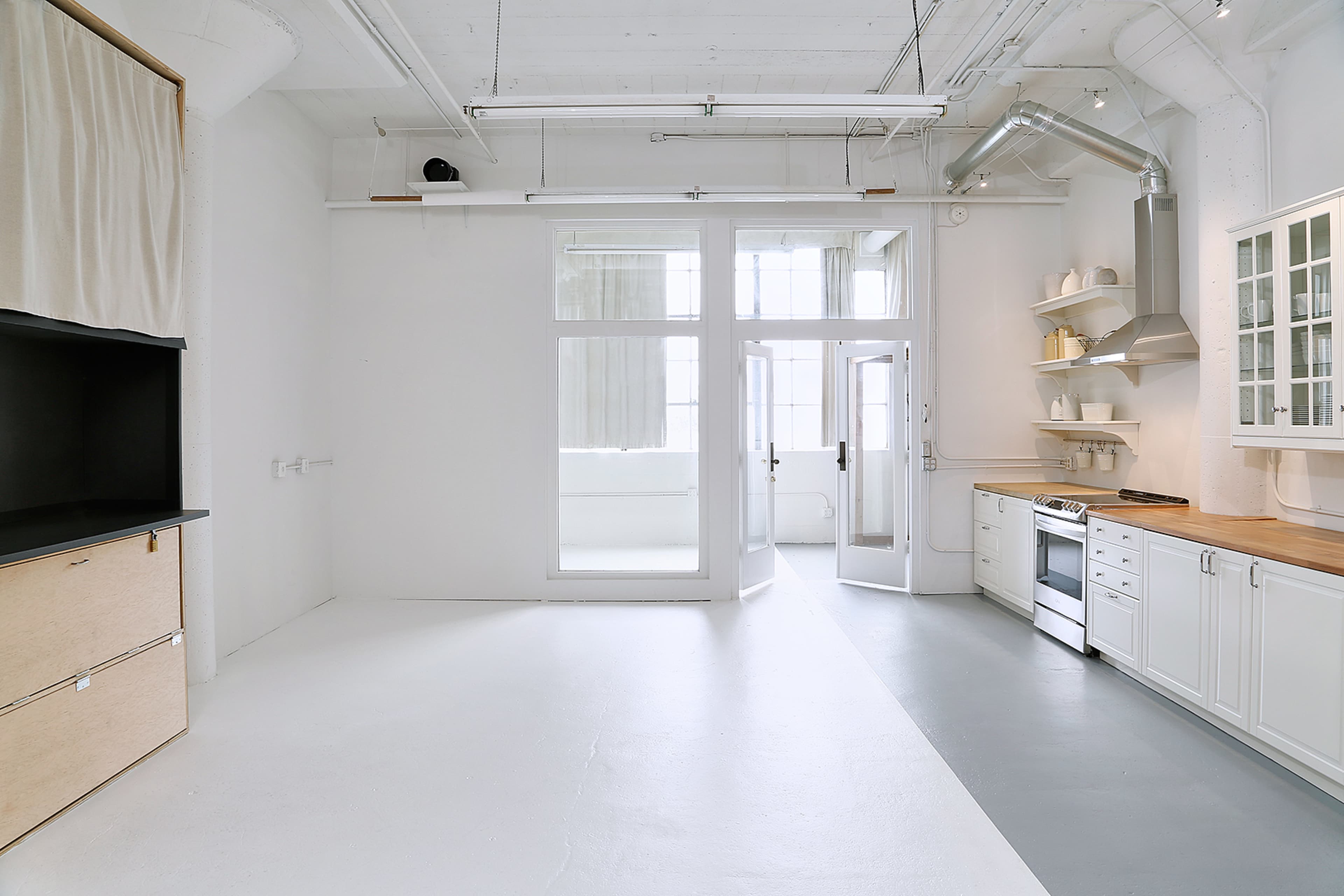 The image shows a modern, open kitchen with white walls, a wooden countertop, and large windows allowing natural light to enter.