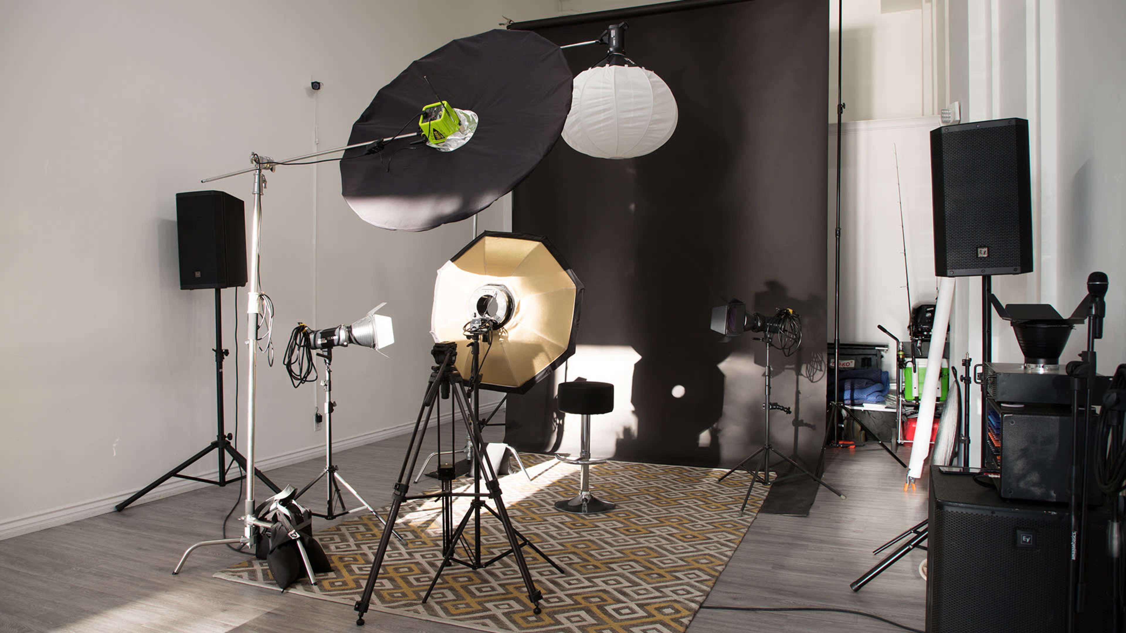 A photography studio set up with various lighting equipment, backdrops, and a stool on a patterned rug.
