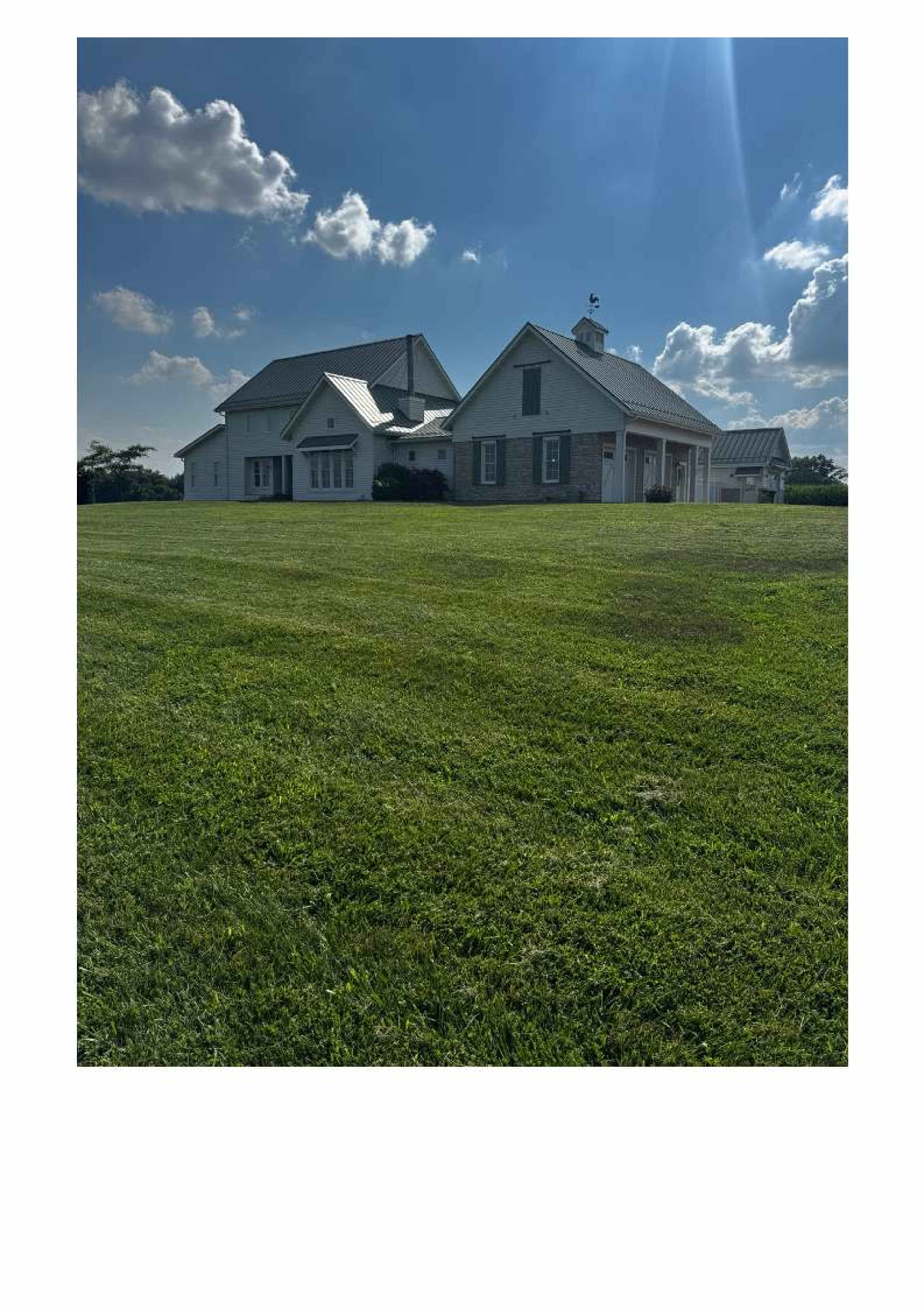 The image shows a large two-story house with a modern design set on a spacious green lawn under a partly cloudy sky.