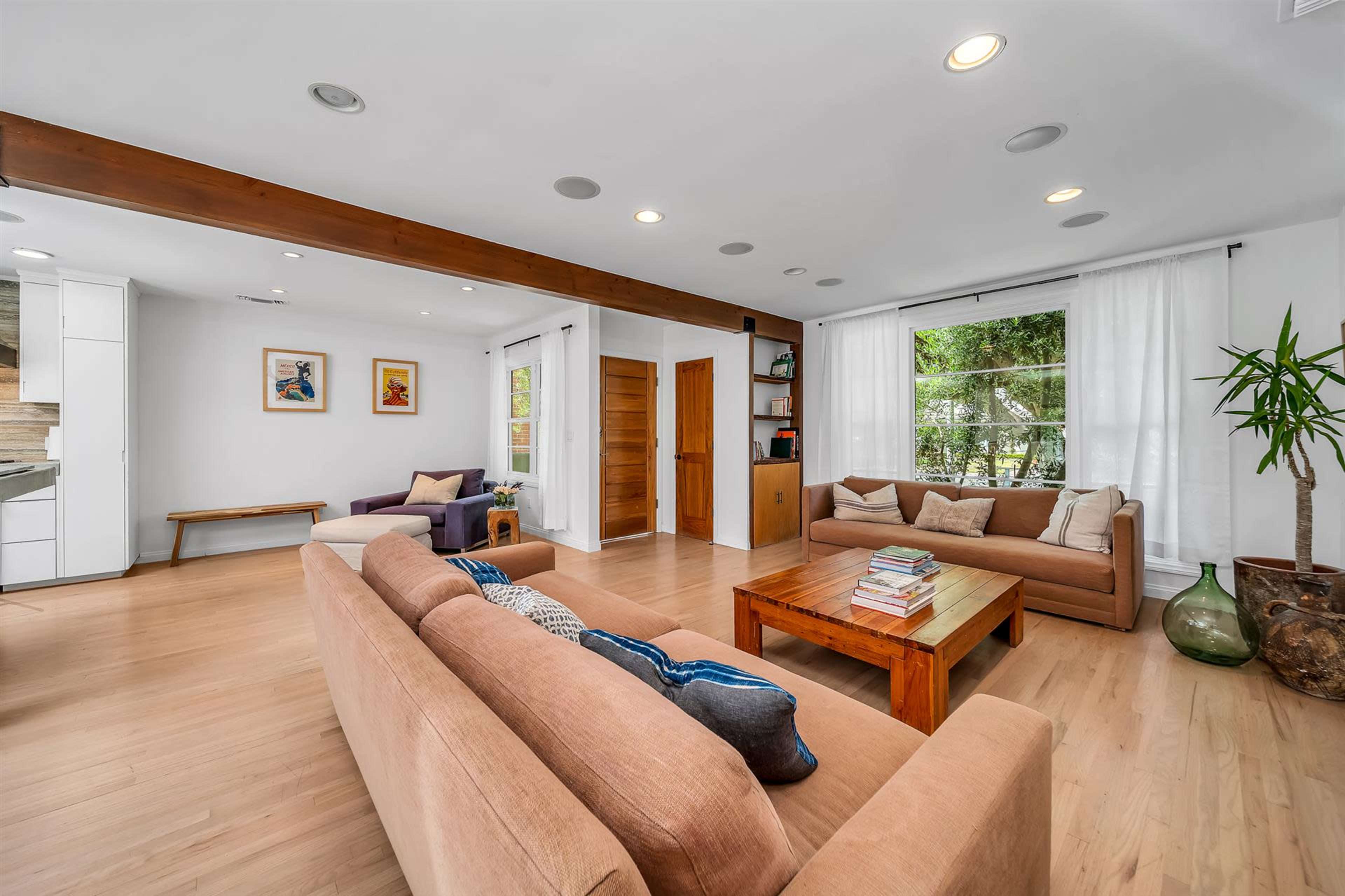 A modern living room with light wooden floors, two sofas, a coffee table, and large windows allowing natural light to enter.
