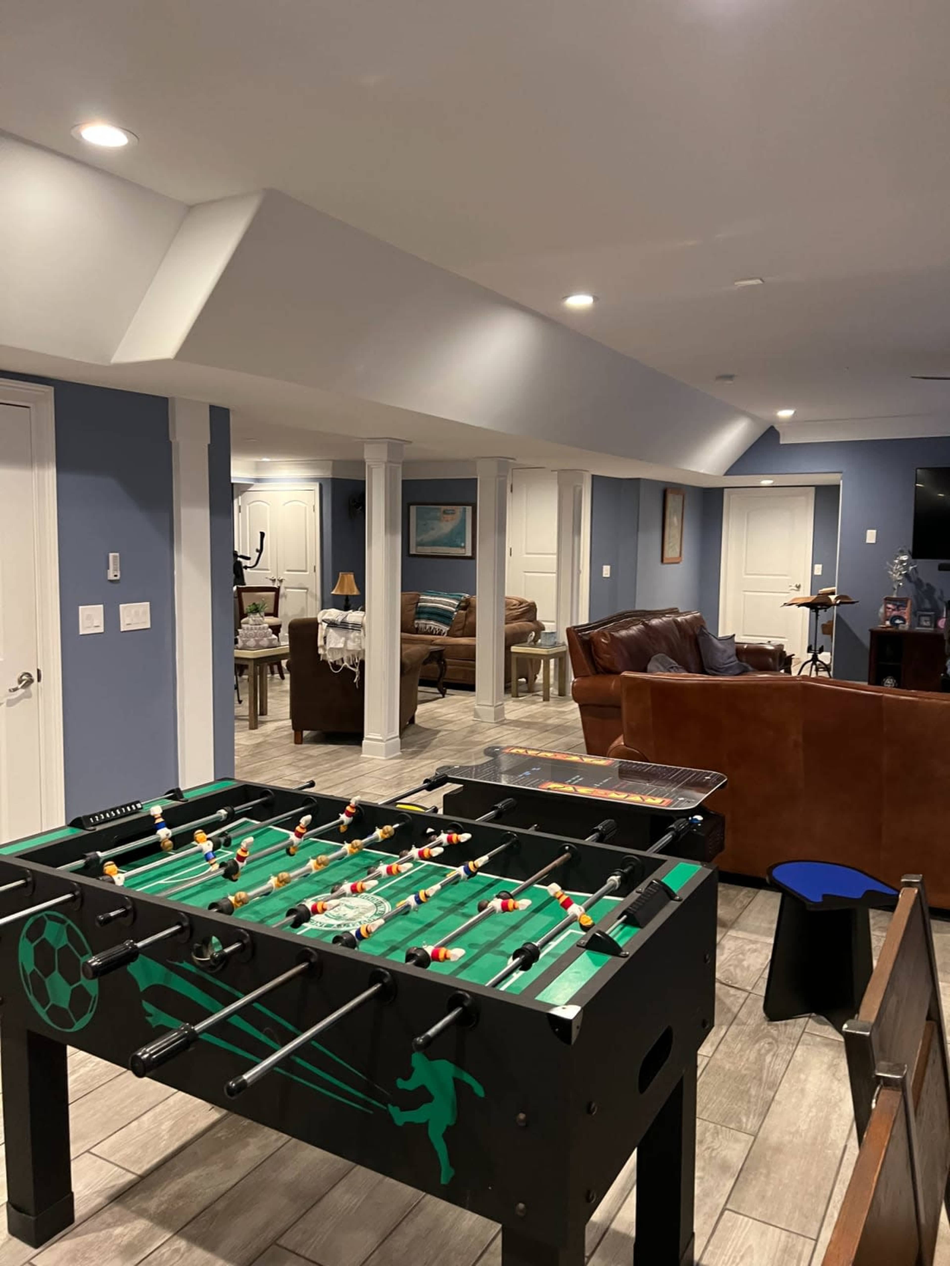 A basement recreation area featuring a foosball table, a seating area with brown couches, and white walls adorned with blue paint.