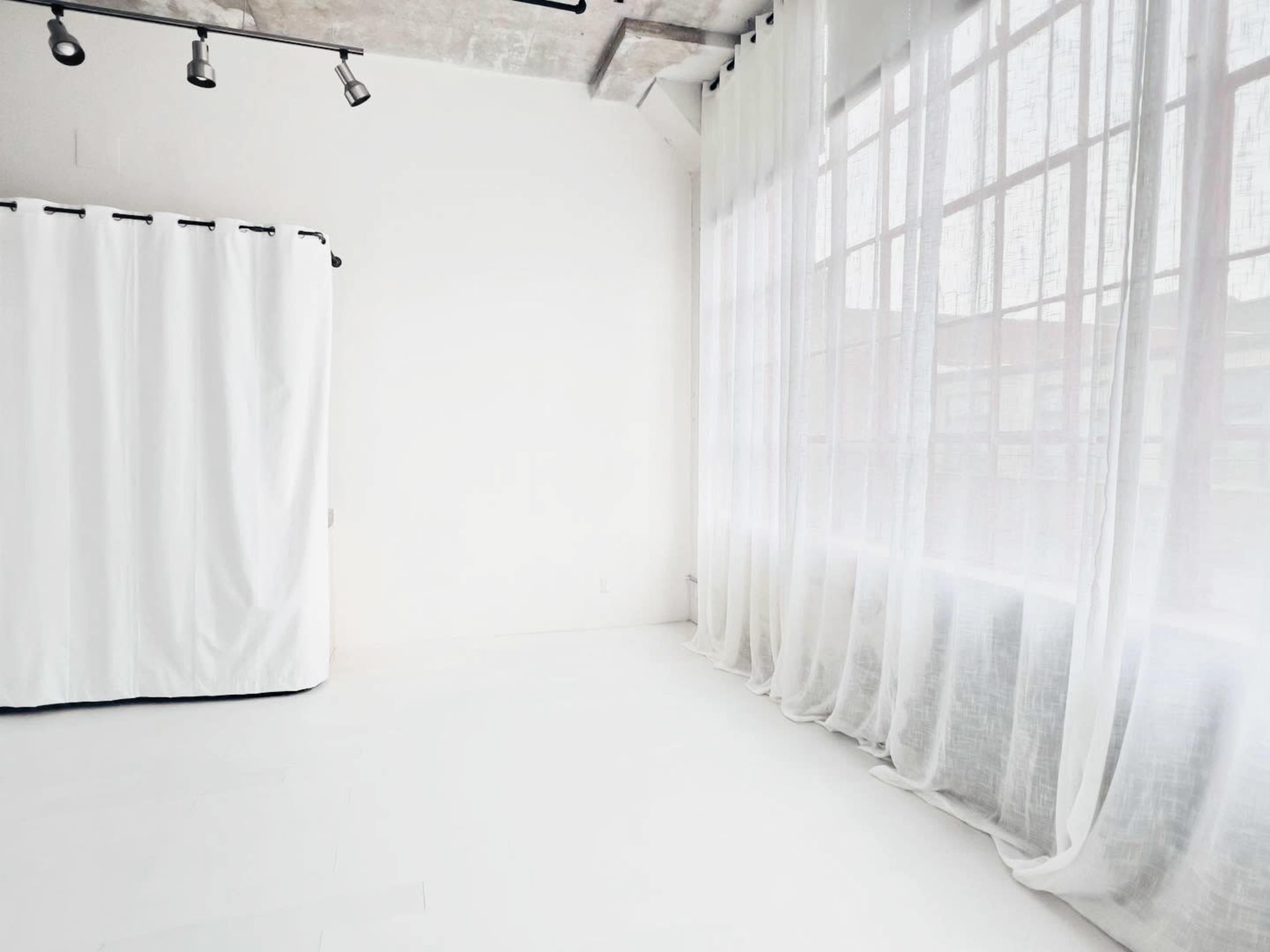 A minimalist room features a large window with sheer curtains and a curtain partition against a white wall.