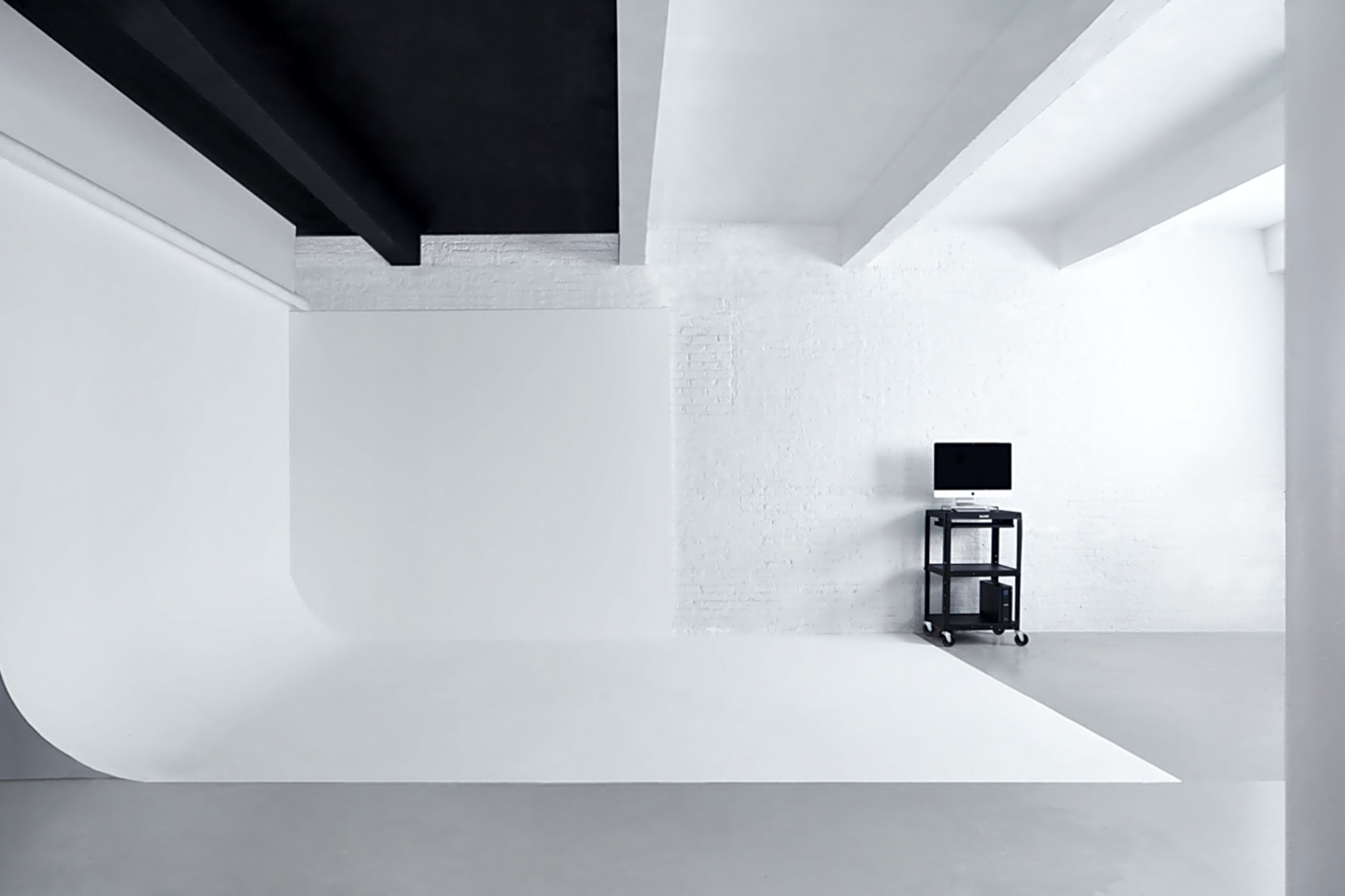 A minimalist room with a seamless white backdrop, a black ceiling, and a small black television on a wheeled cart.