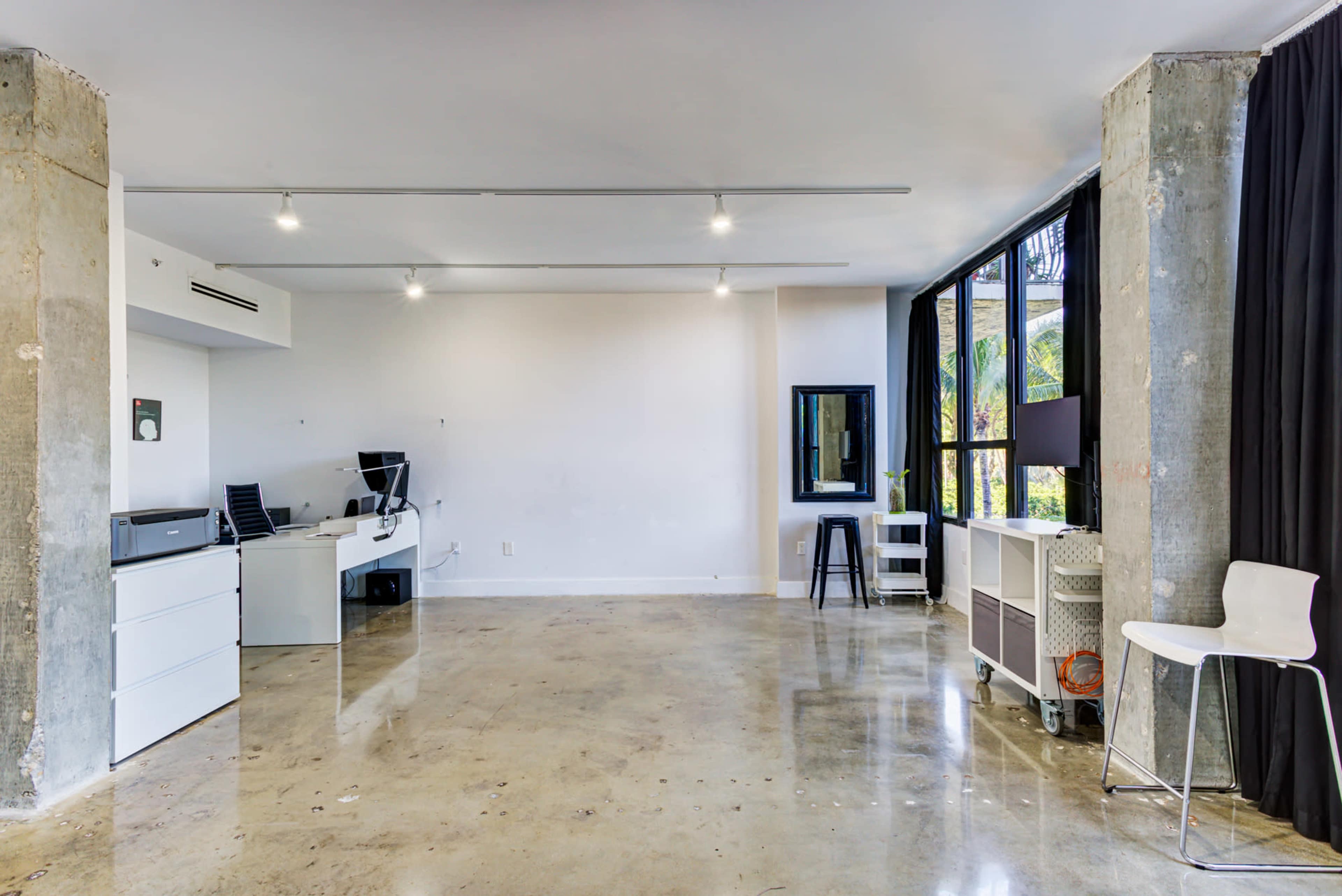 An open office space with polished concrete floors, a desk and office chair, and large windows allowing natural light.