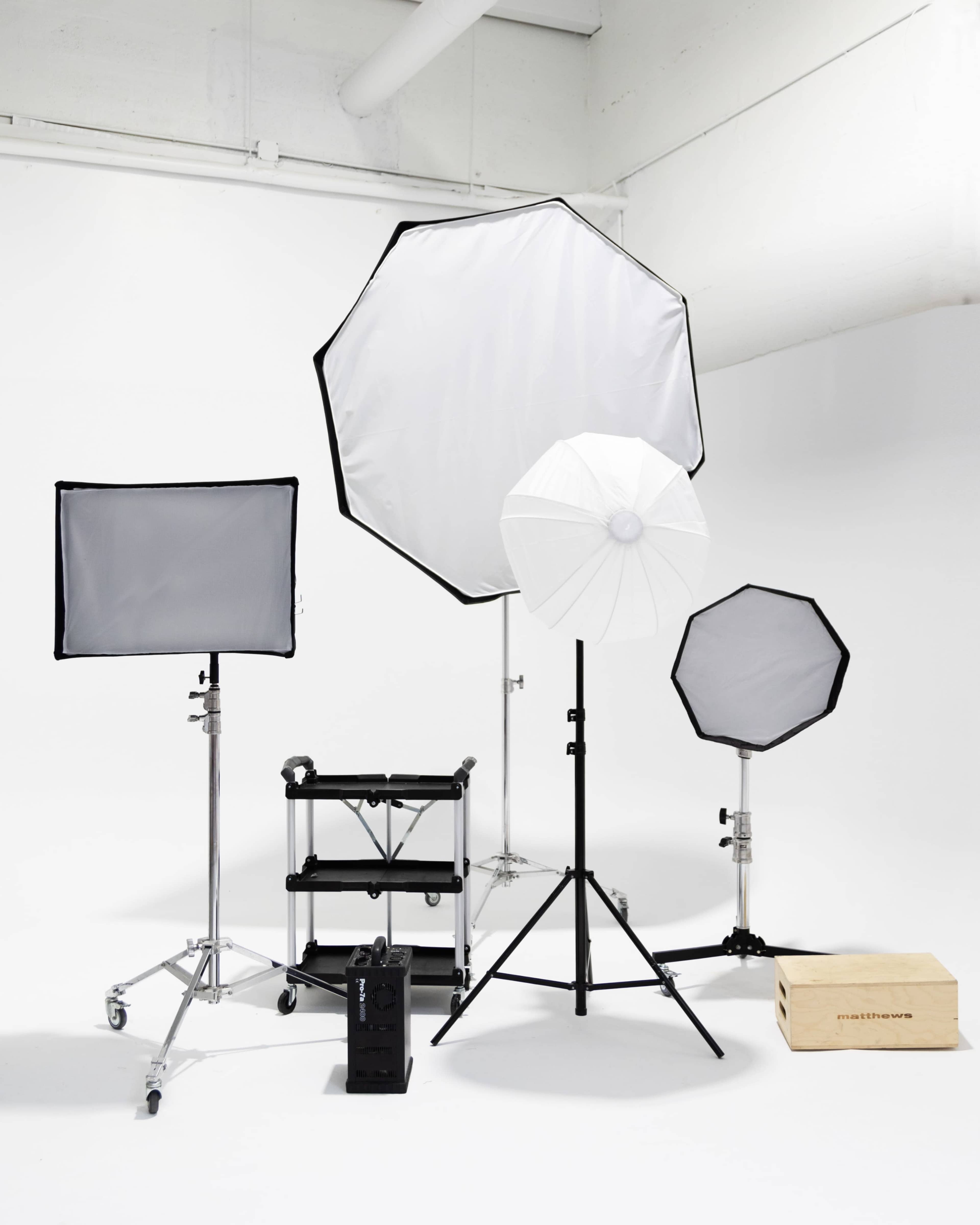 A collection of photography lighting equipment arranged in a studio setting, including softboxes, umbrellas, and a light stand on a minimalistic white background.