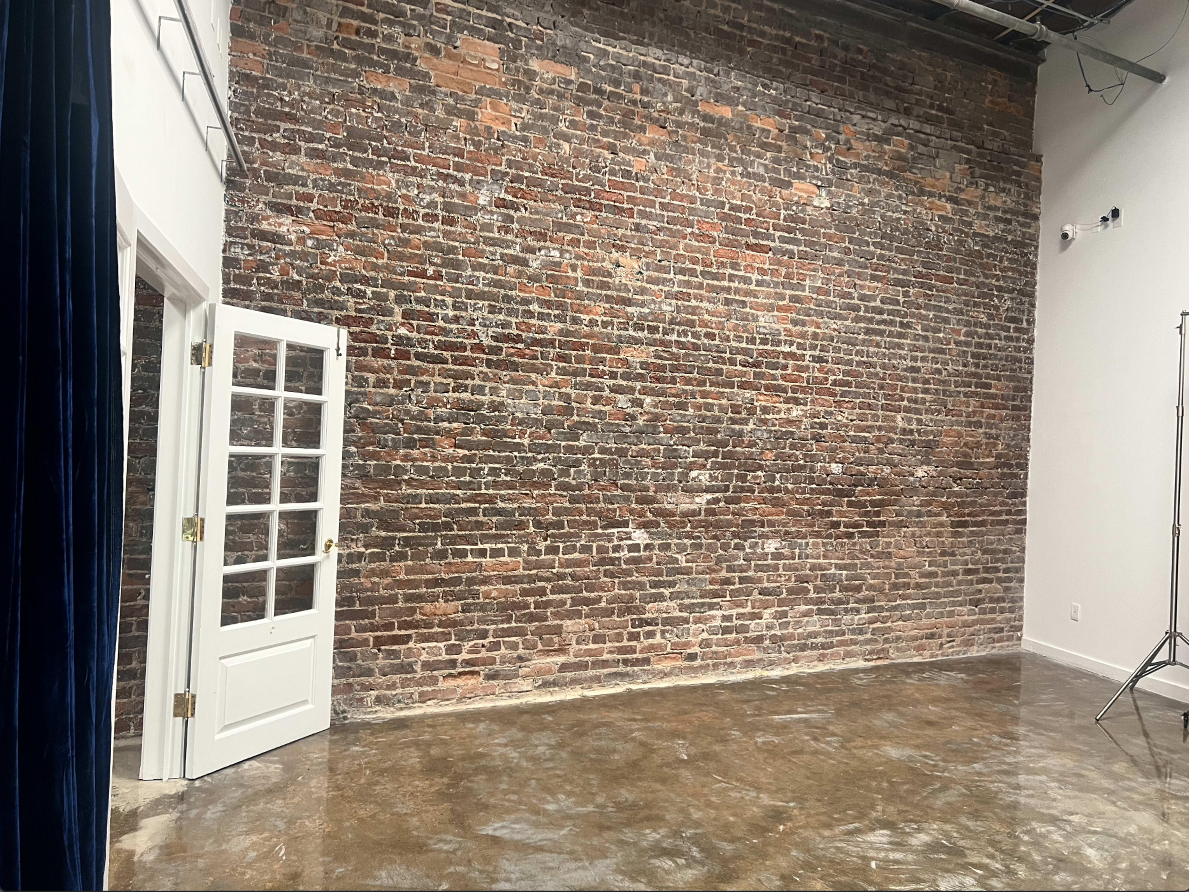 The image shows an interior space with a brick wall, polished concrete flooring, and a white door partially open.