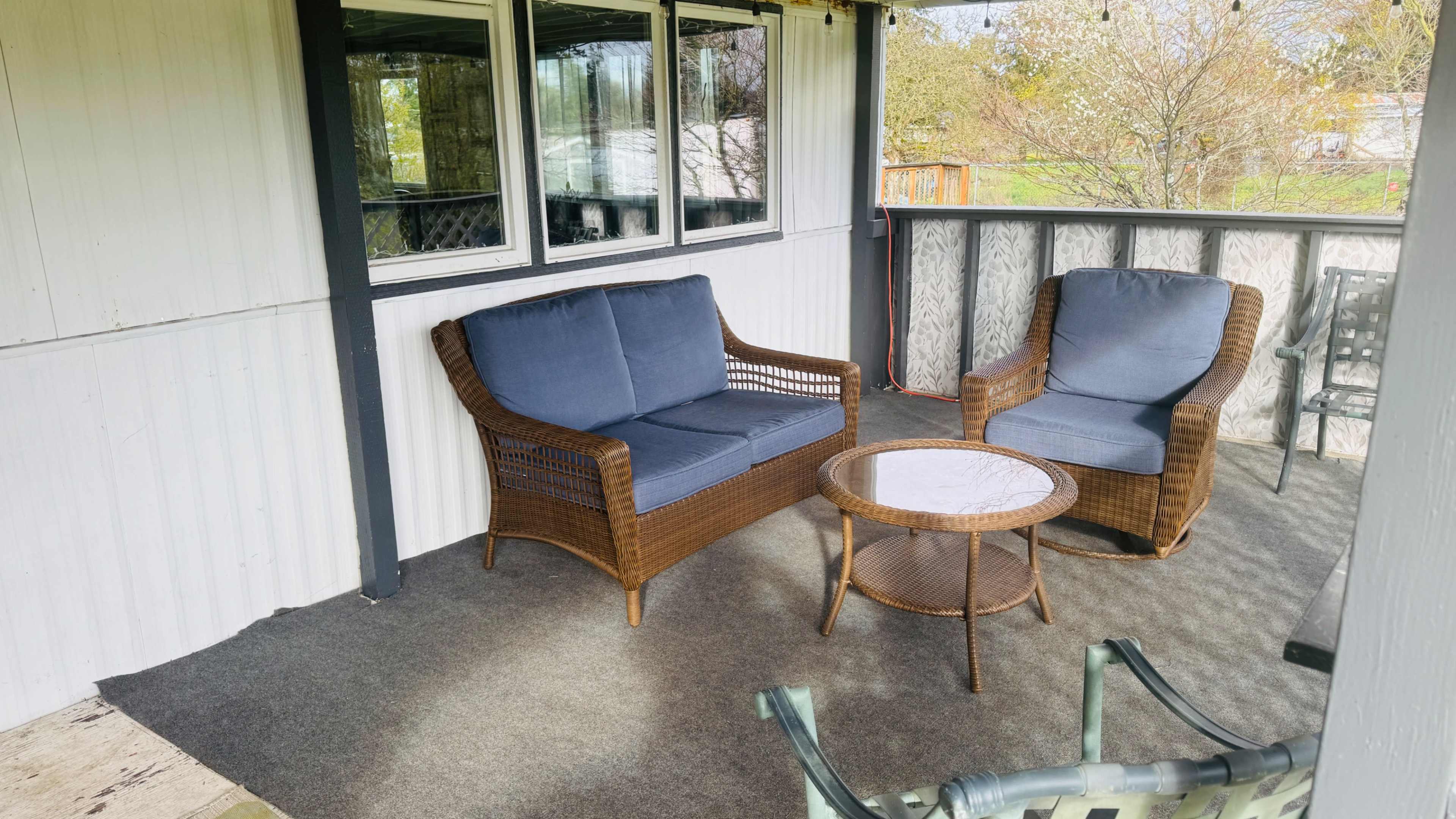 The image shows a small outdoor seating area with two wicker chairs and a round table on a covered porch.