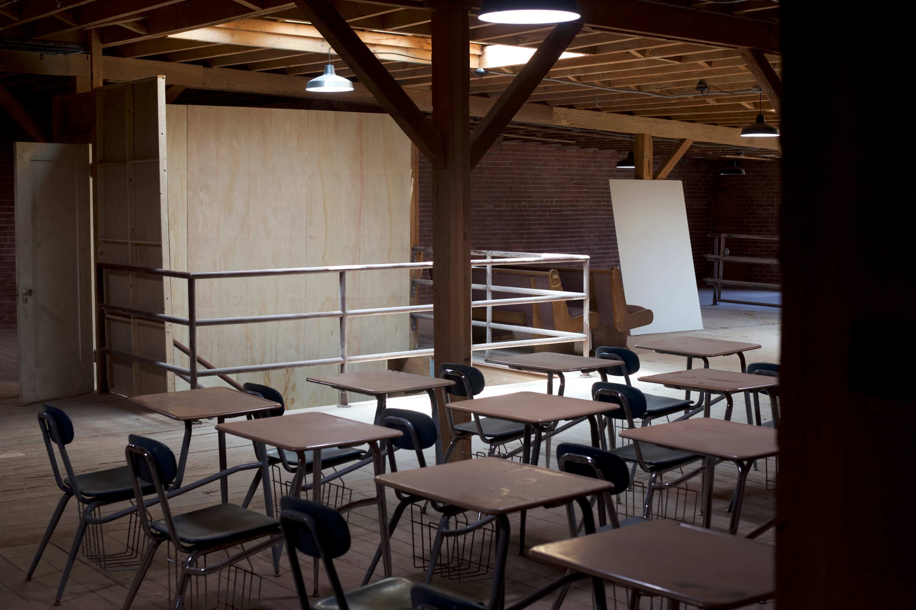 An empty classroom with wooden desks arranged in rows and wooden beams supporting the ceiling.