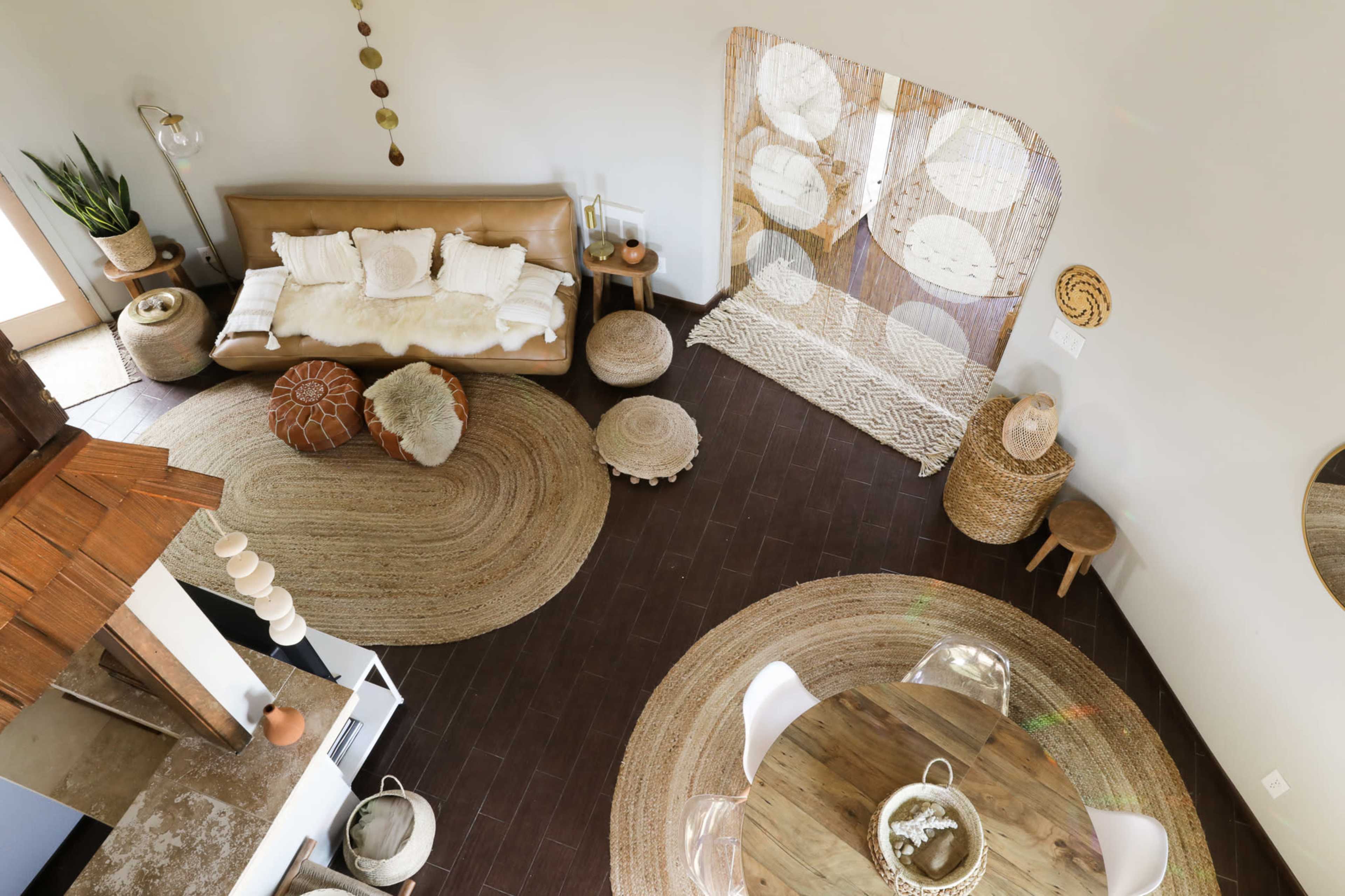 A cozy living room with a brown leather sofa, woven decorations, and various round rugs and stools arranged on a dark floor.