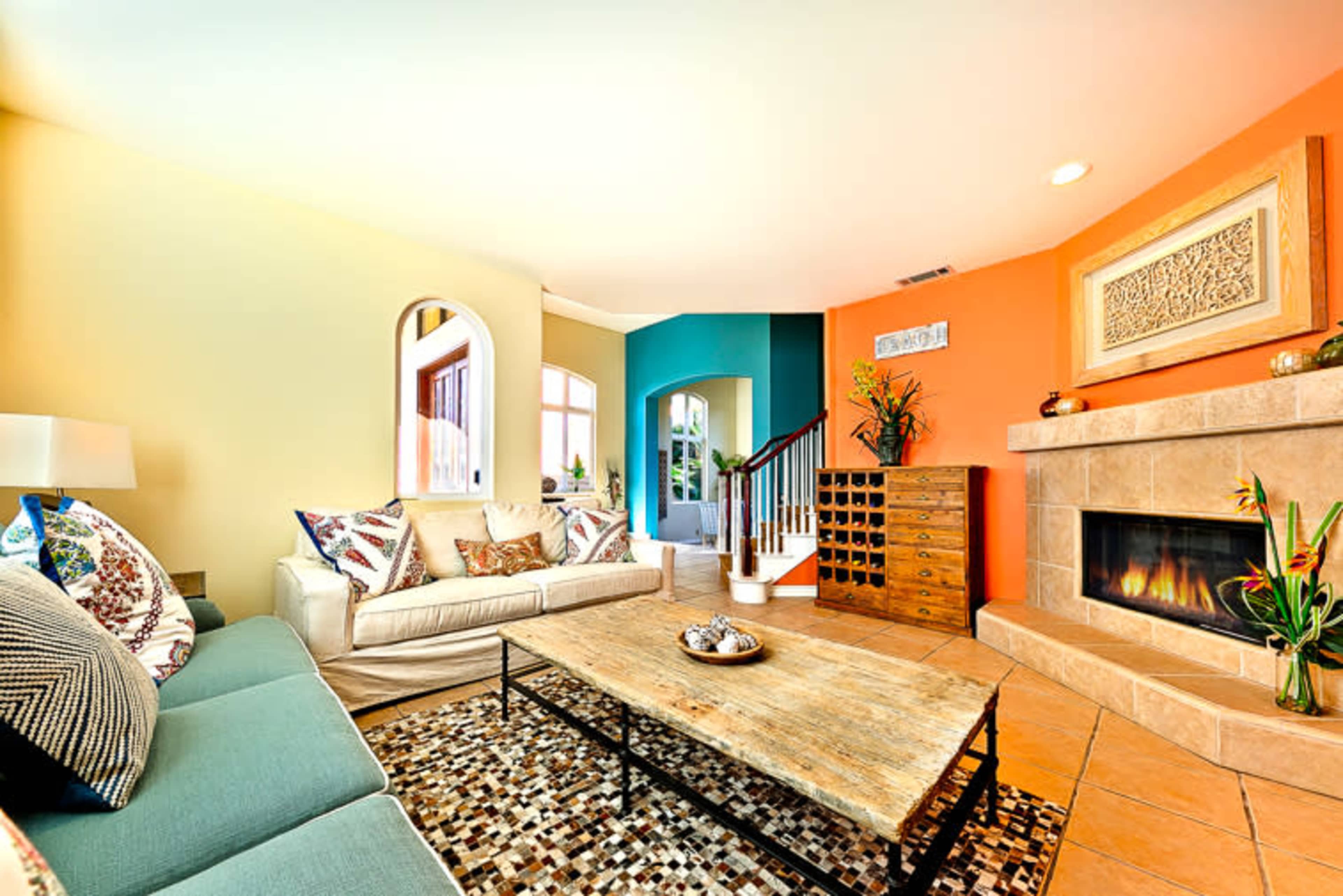 The living room features a beige sofa and a blue accent chair surrounding a wooden coffee table, with a stone fireplace and colorful walls.