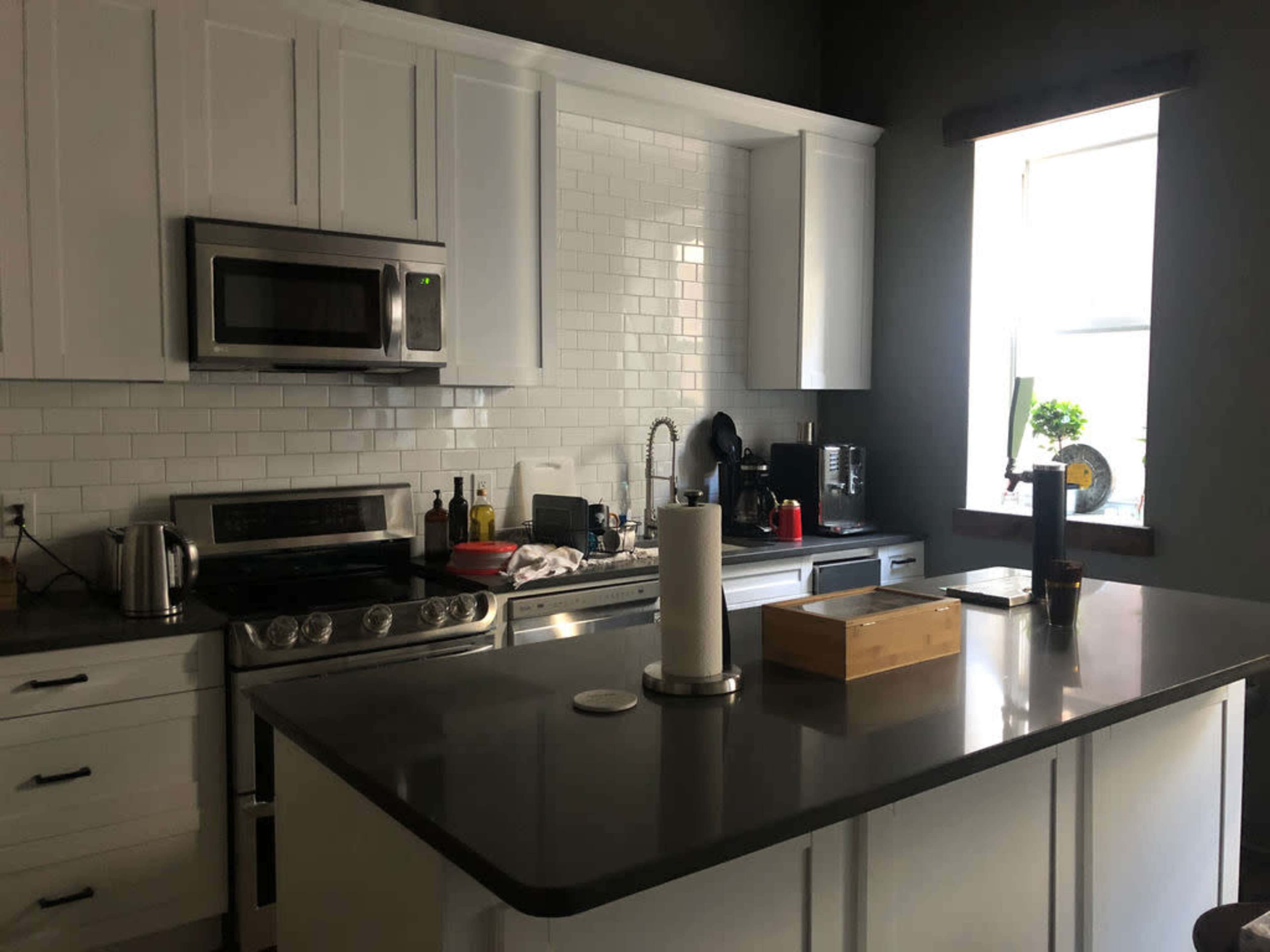 The kitchen features white cabinetry, stainless steel appliances, and a dark countertop with a wooden box and paper towel holder on the island.