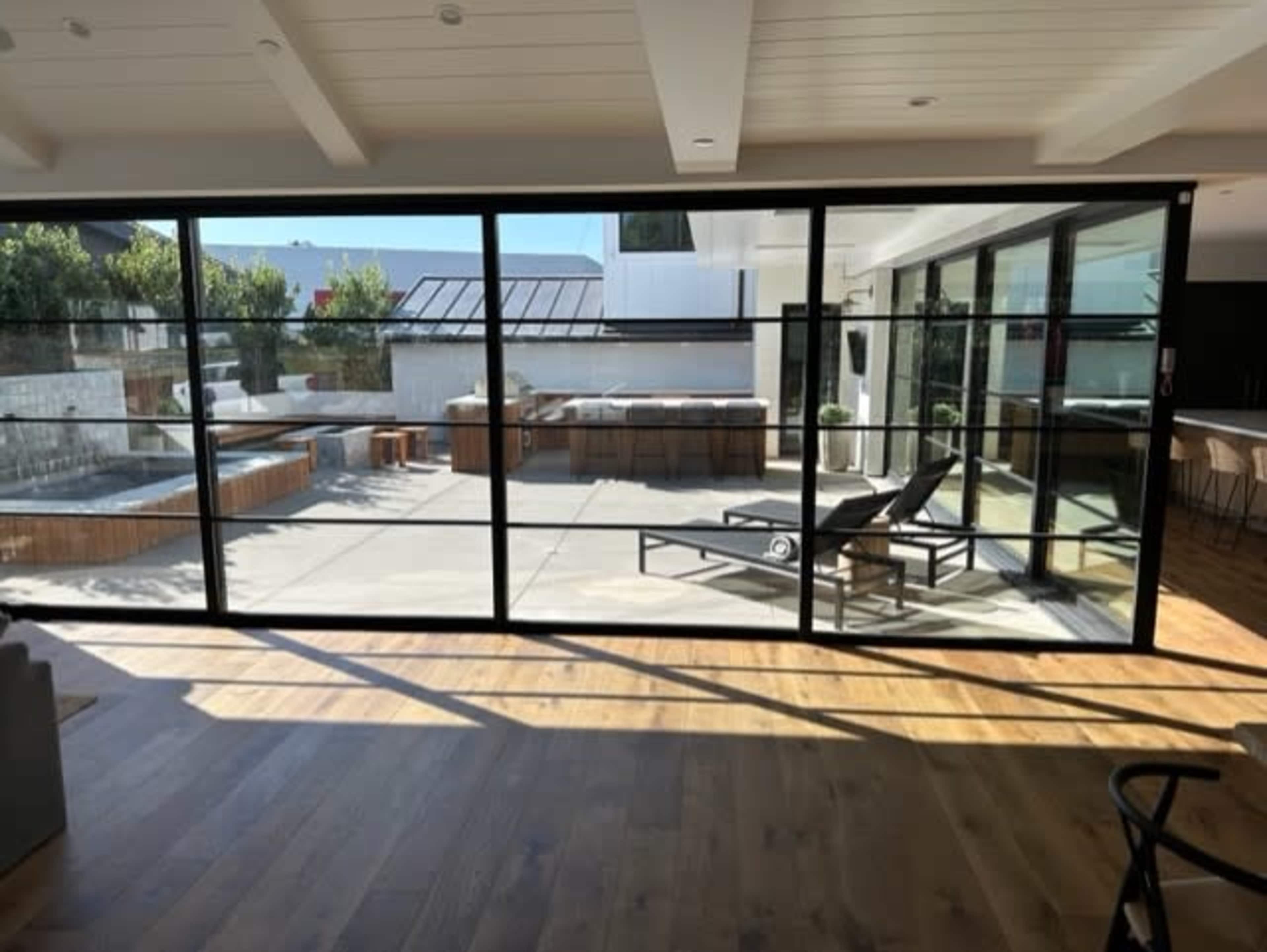 A modern interior space with large glass doors that open to a patio featuring lounge chairs and a pool.