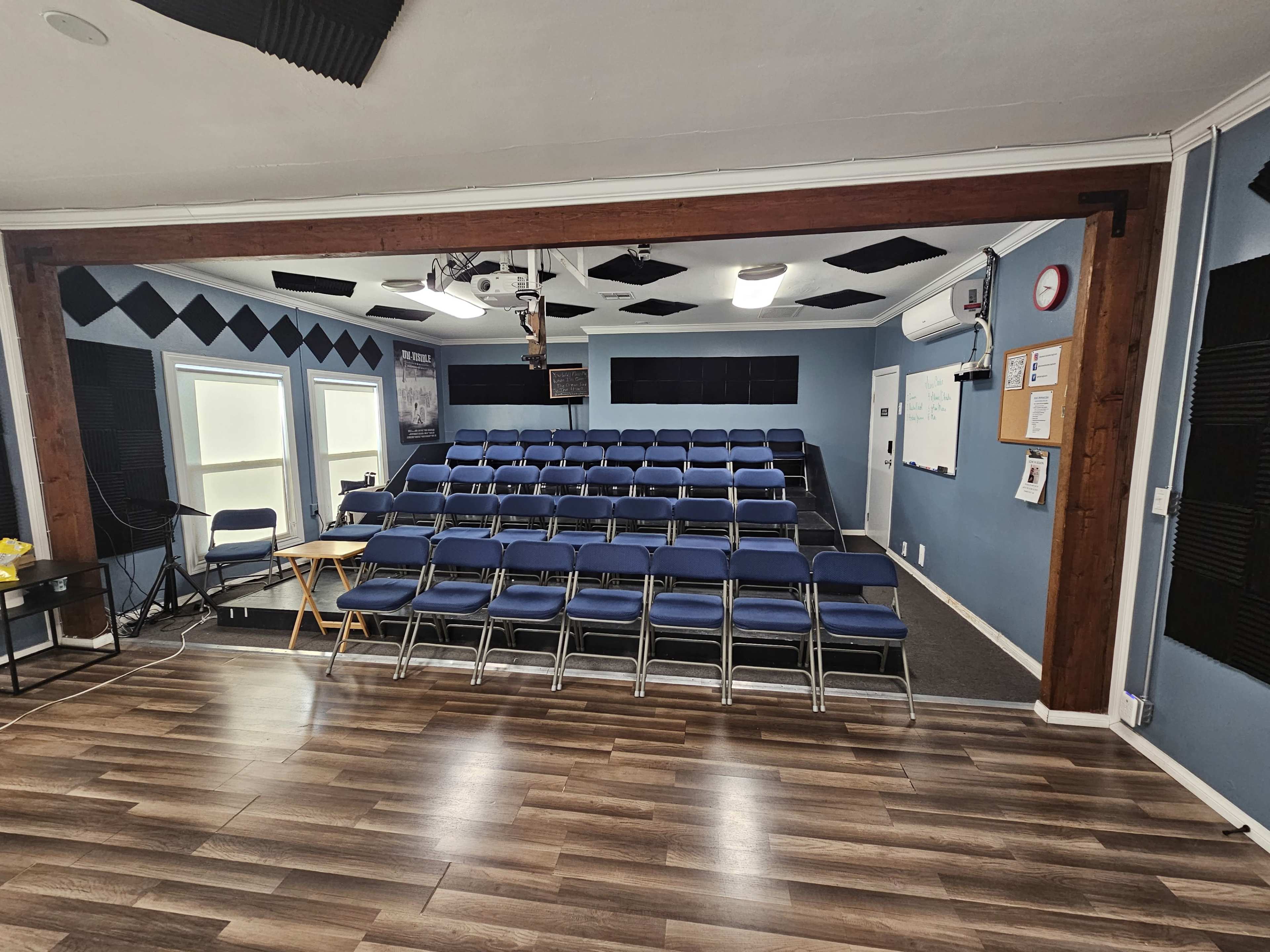 The image shows a seminar room with rows of blue chairs arranged for an audience, a projector mounted on the ceiling, and a whiteboard at the front.