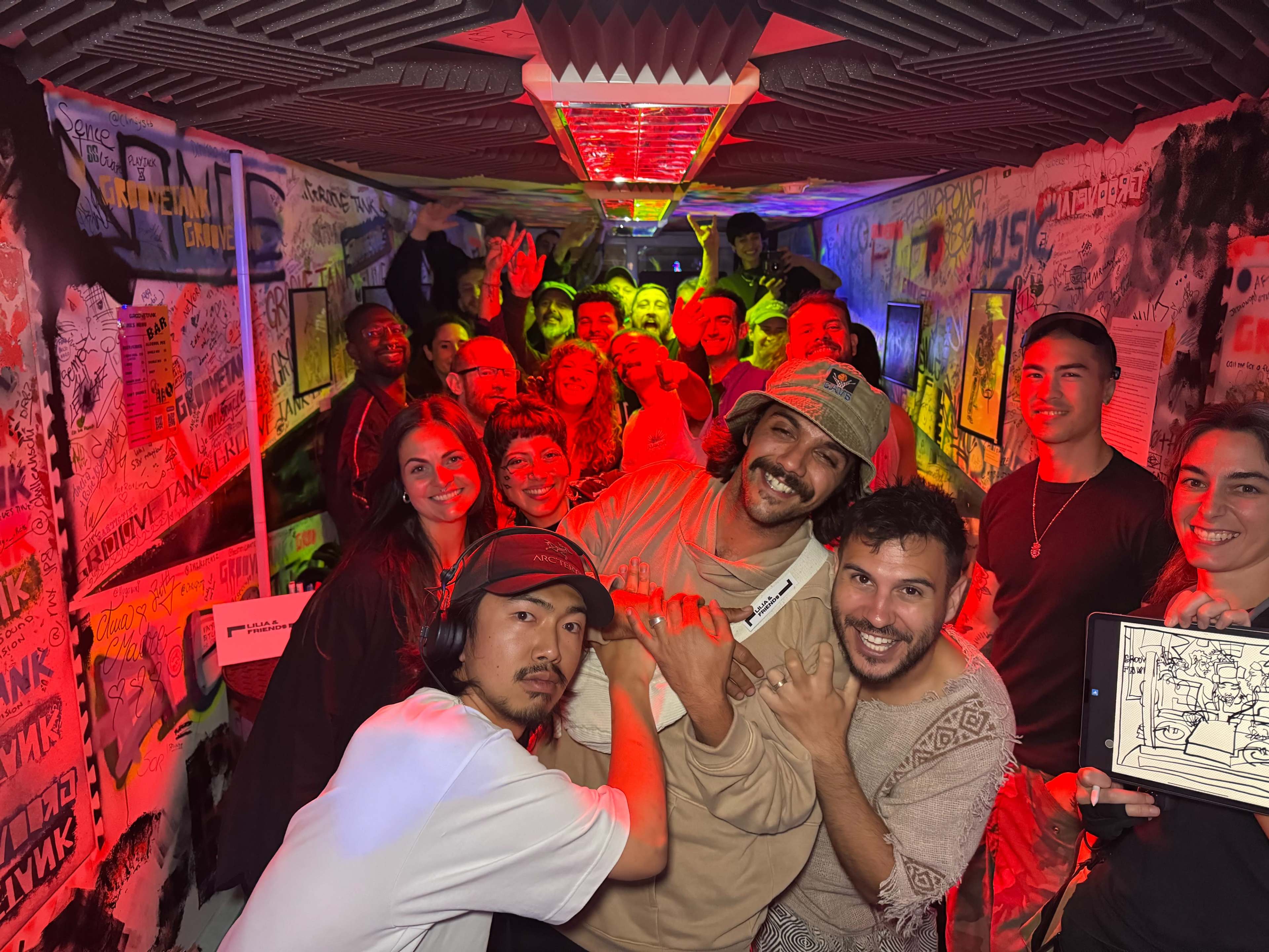 A large group of people poses and smiles for a photo in a colorful, artistically decorated room filled with graffiti and vibrant lighting.