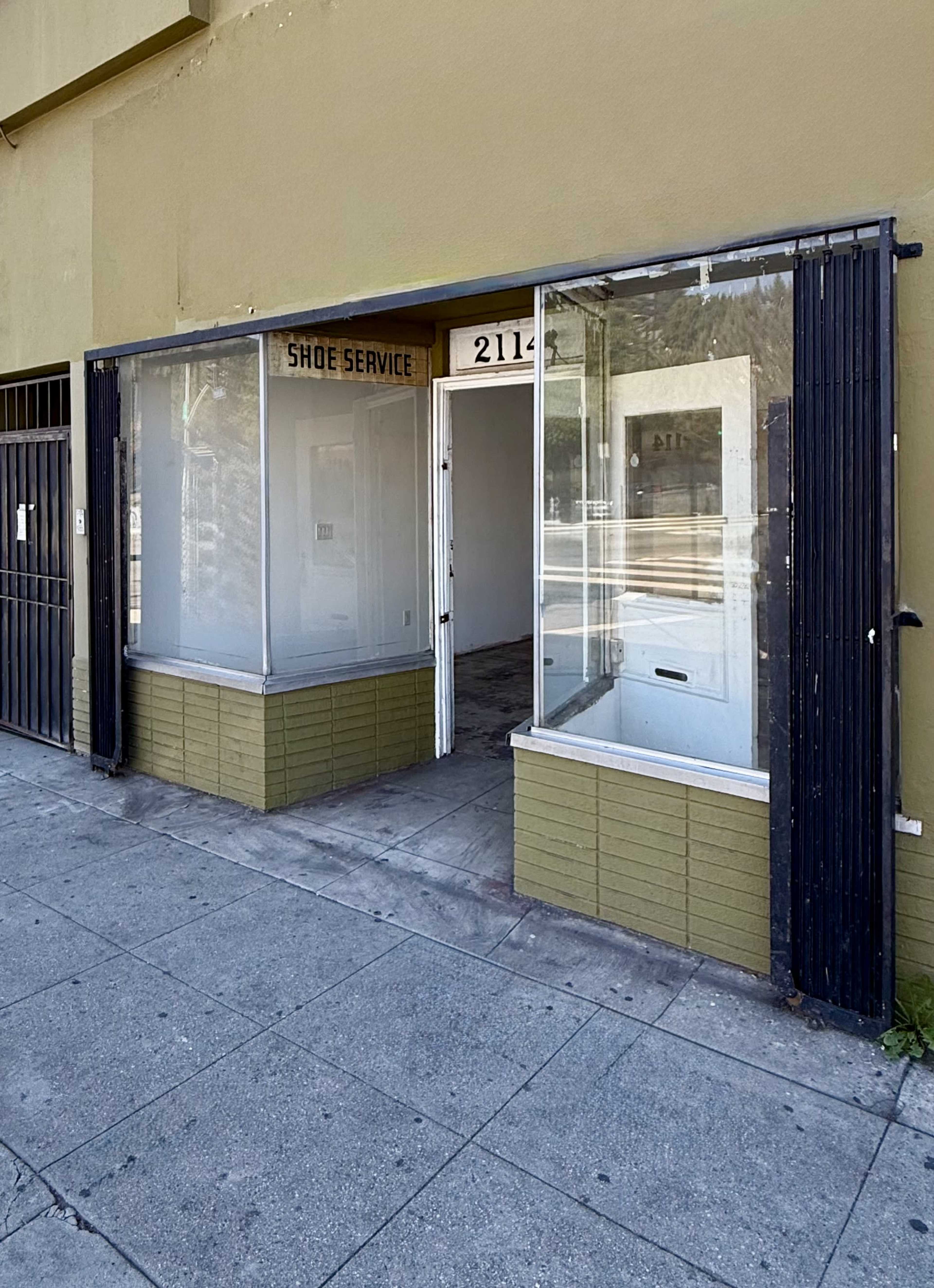 The image shows an empty storefront with large glass windows and a sign that reads "Shoe Service" above the entrance.