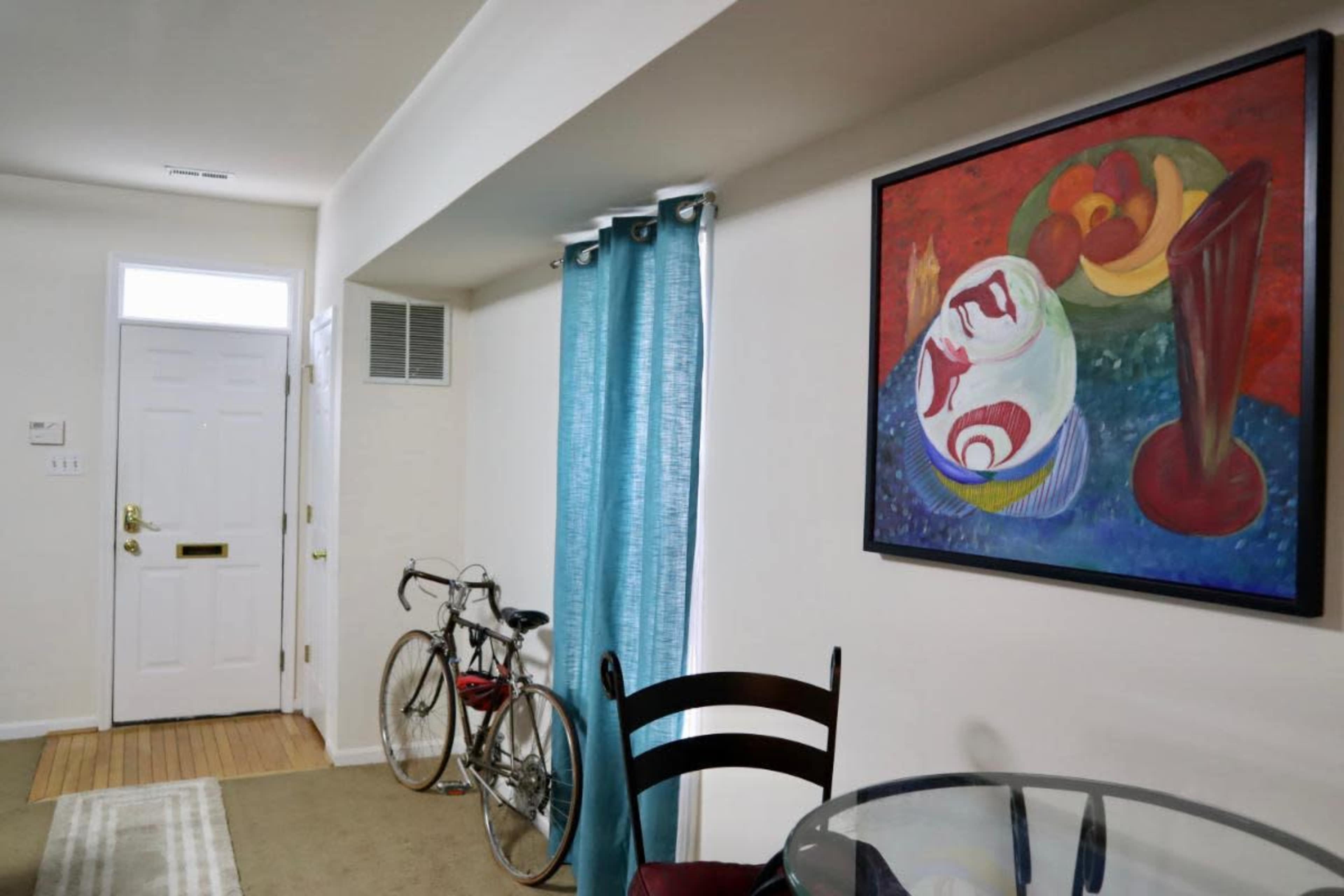 A bicycle is parked near a dining table in a room featuring a colorful painting and a door leading outside.