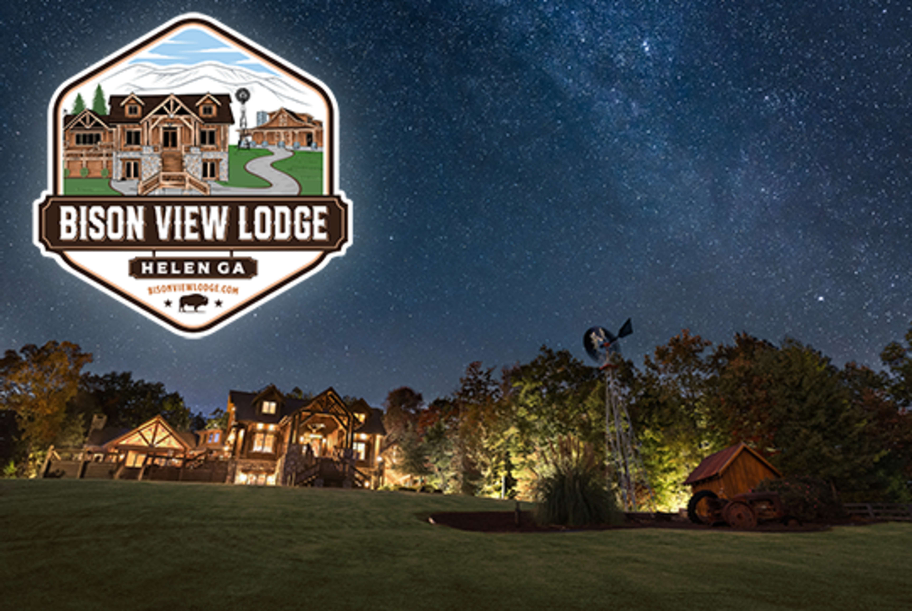 The Bison View Lodge in Helen, GA, set against a starry night sky, with a windmill and rustic equipment in the foreground.