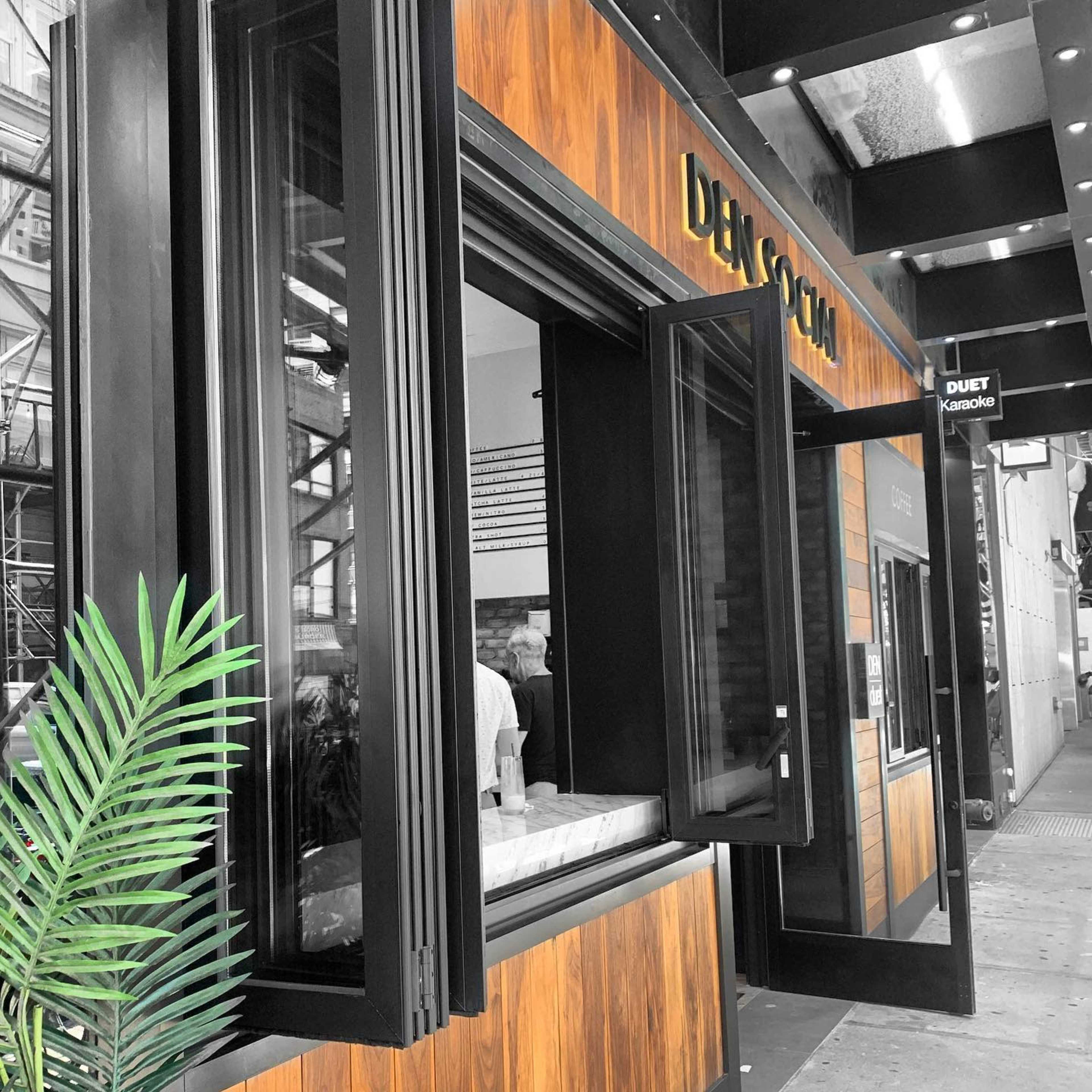 A restaurant with large windows displaying a wooden facade and a small palm plant at the entrance.