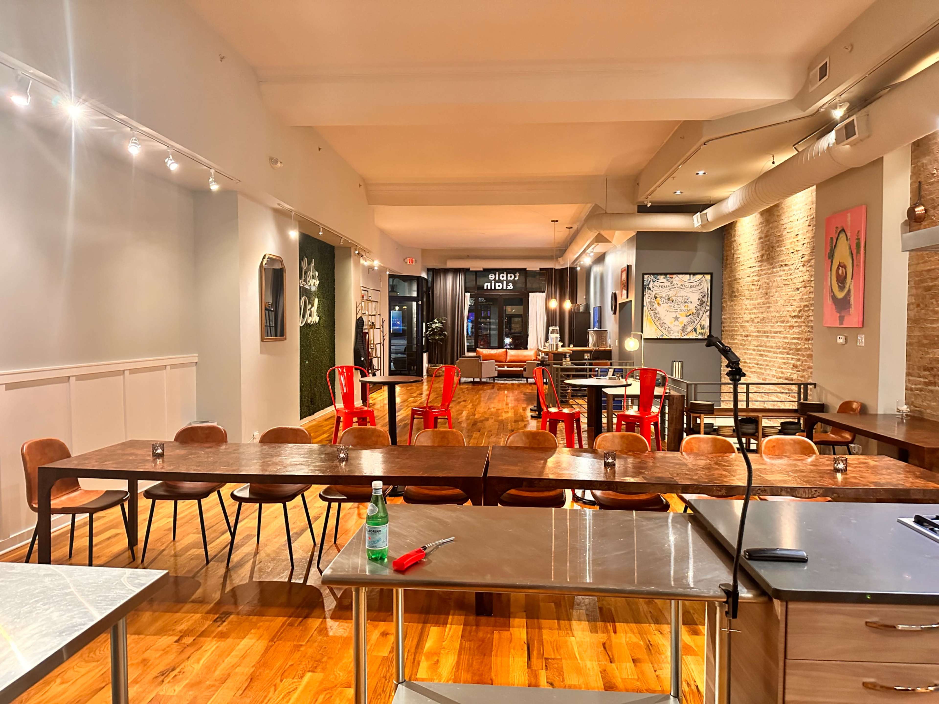 The image shows a spacious restaurant with wooden flooring, various tables and chairs, and a large window at the back.