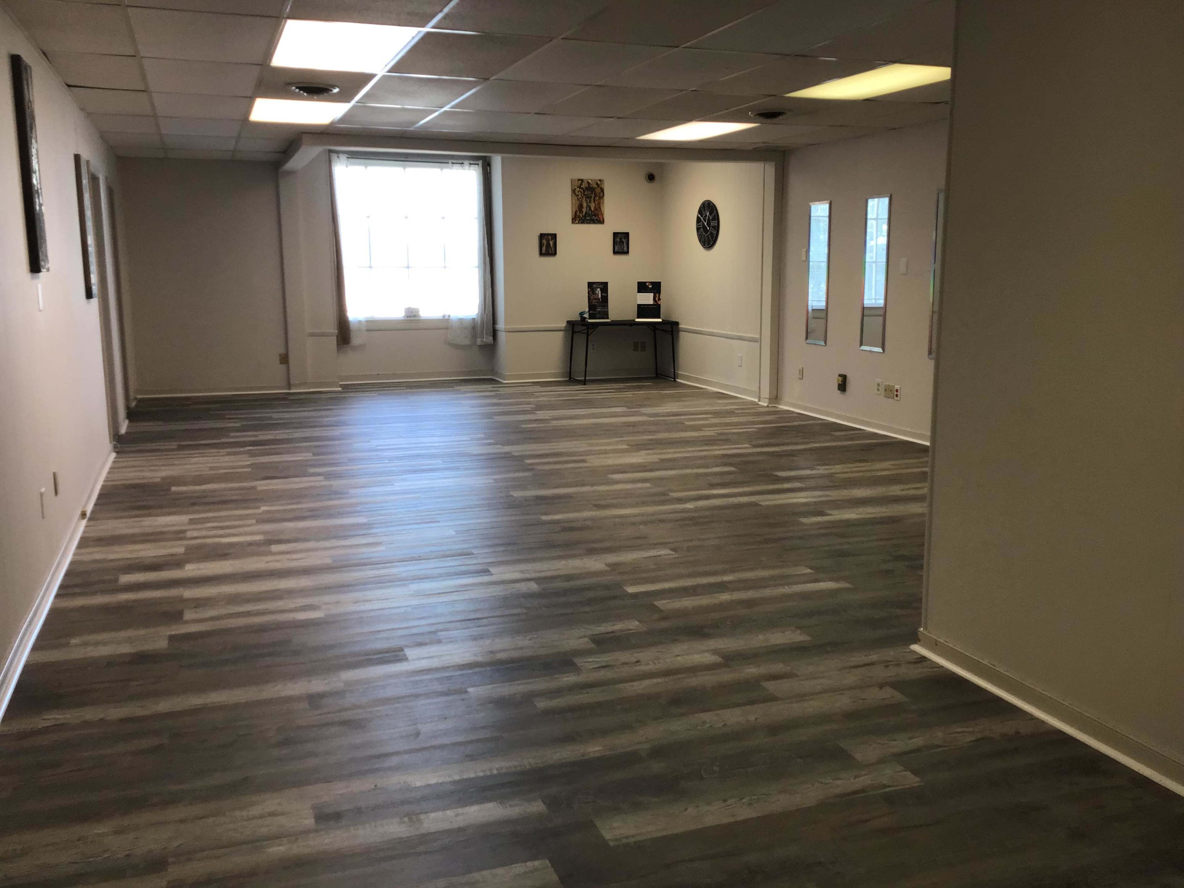 A spacious, empty room with a hardwood floor and windows allowing natural light.