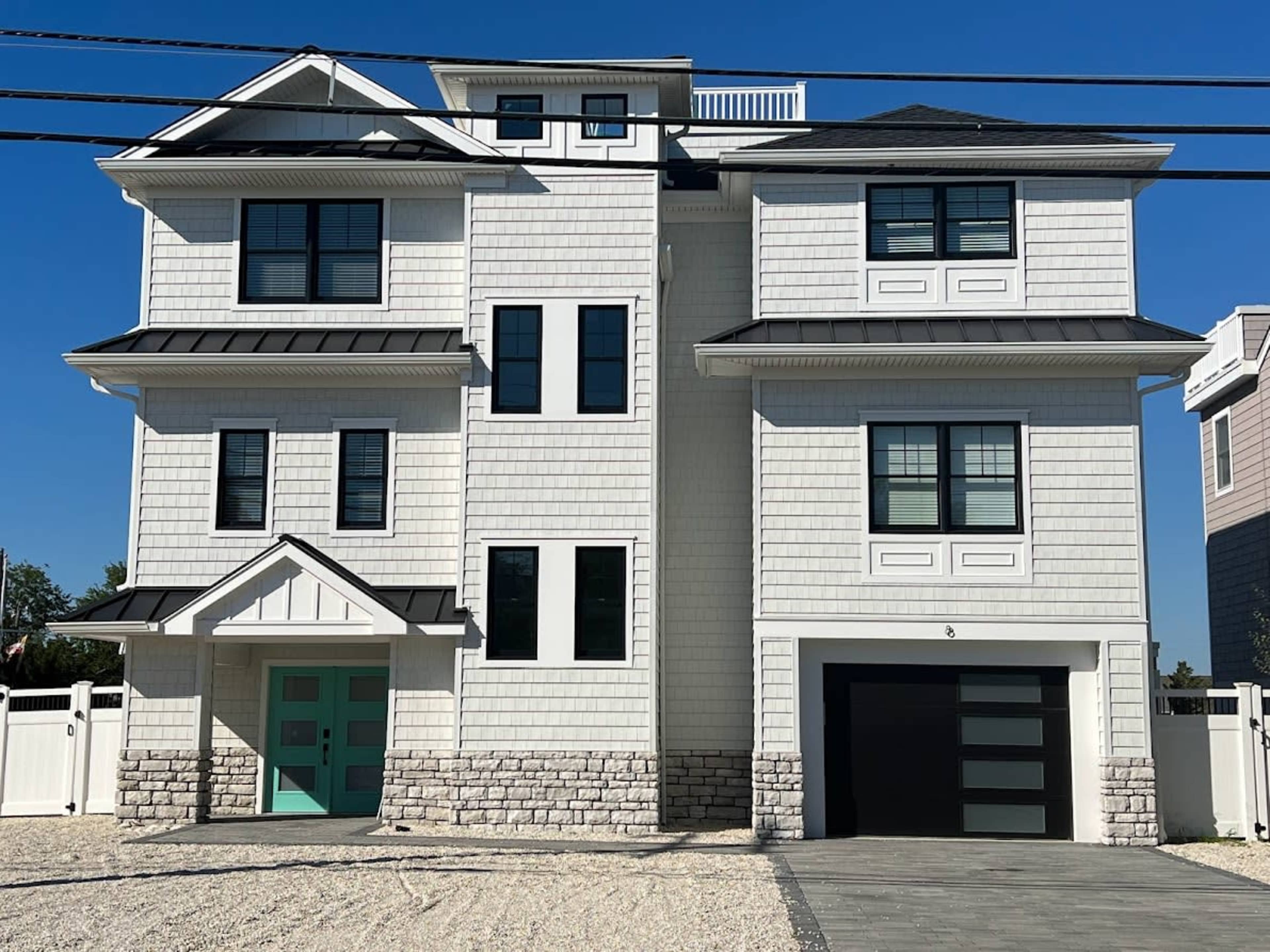 The image shows a modern multi-story house with a white exterior and stone accents, featuring a two-car garage and a bright teal front door.