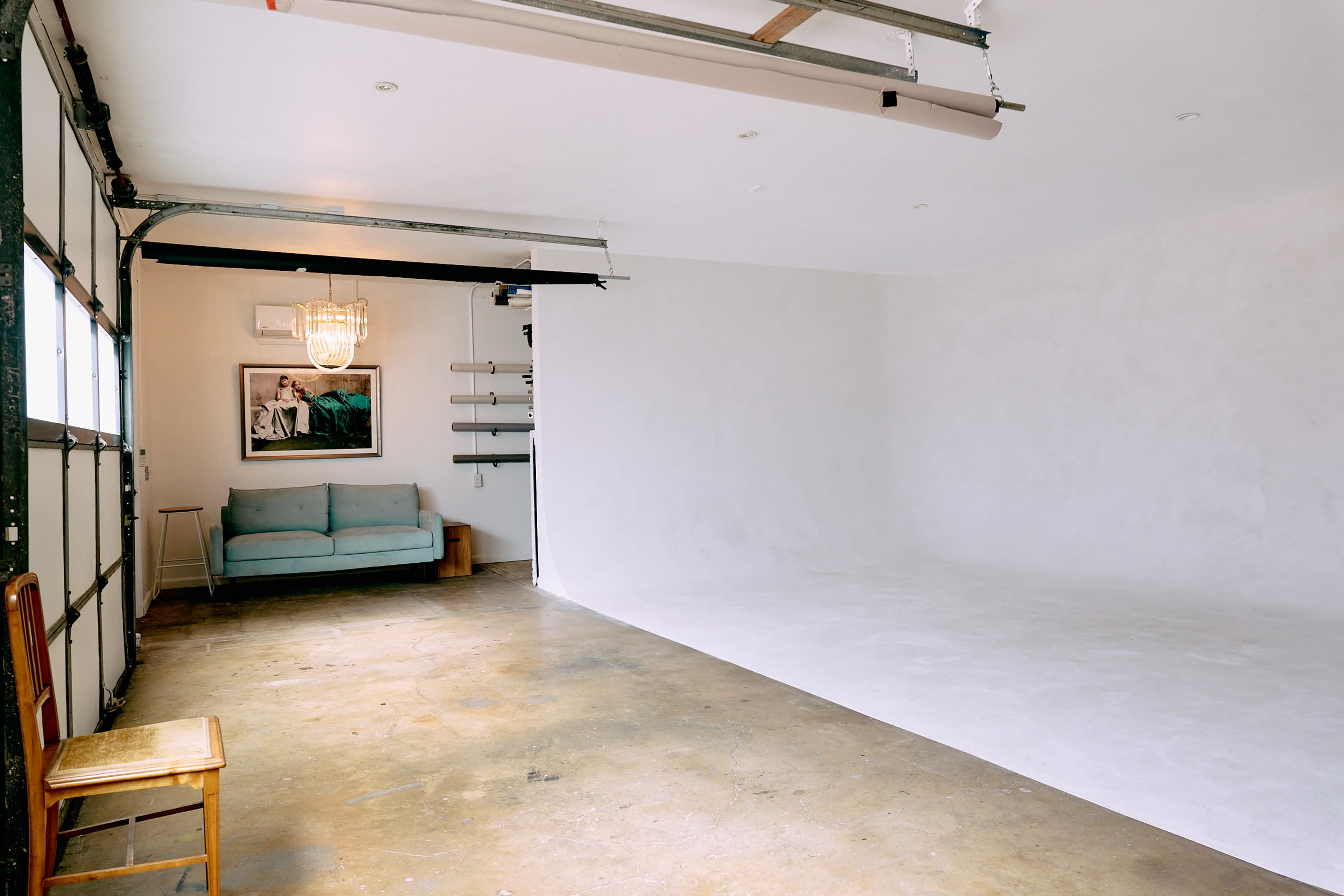 A spacious, empty studio features a light-colored wall, polished concrete floor, and a blue sofa in one corner.