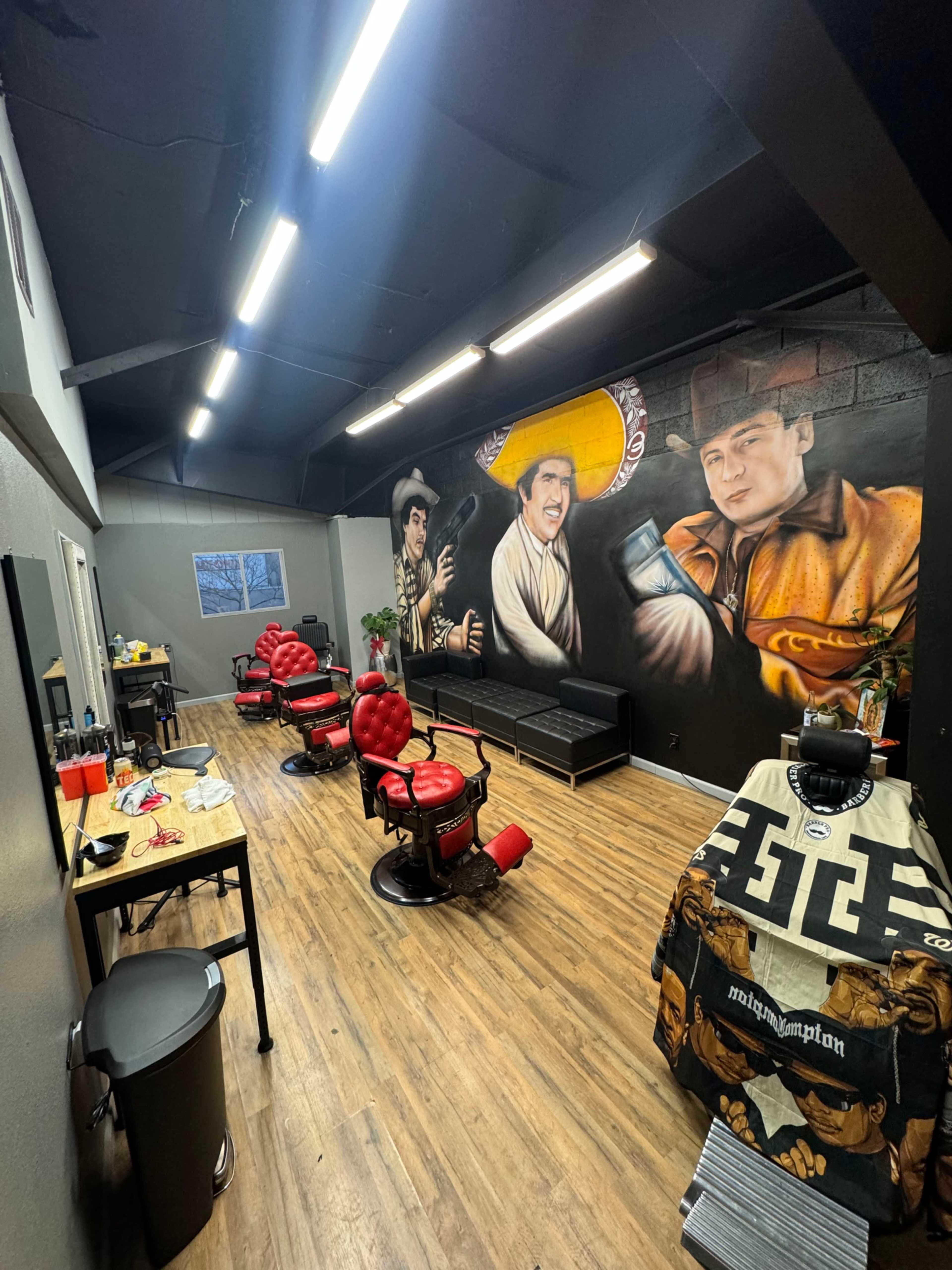 The interior of a tattoo parlor features red barber chairs, a black sofa, and a mural depicting three characters on the wall.