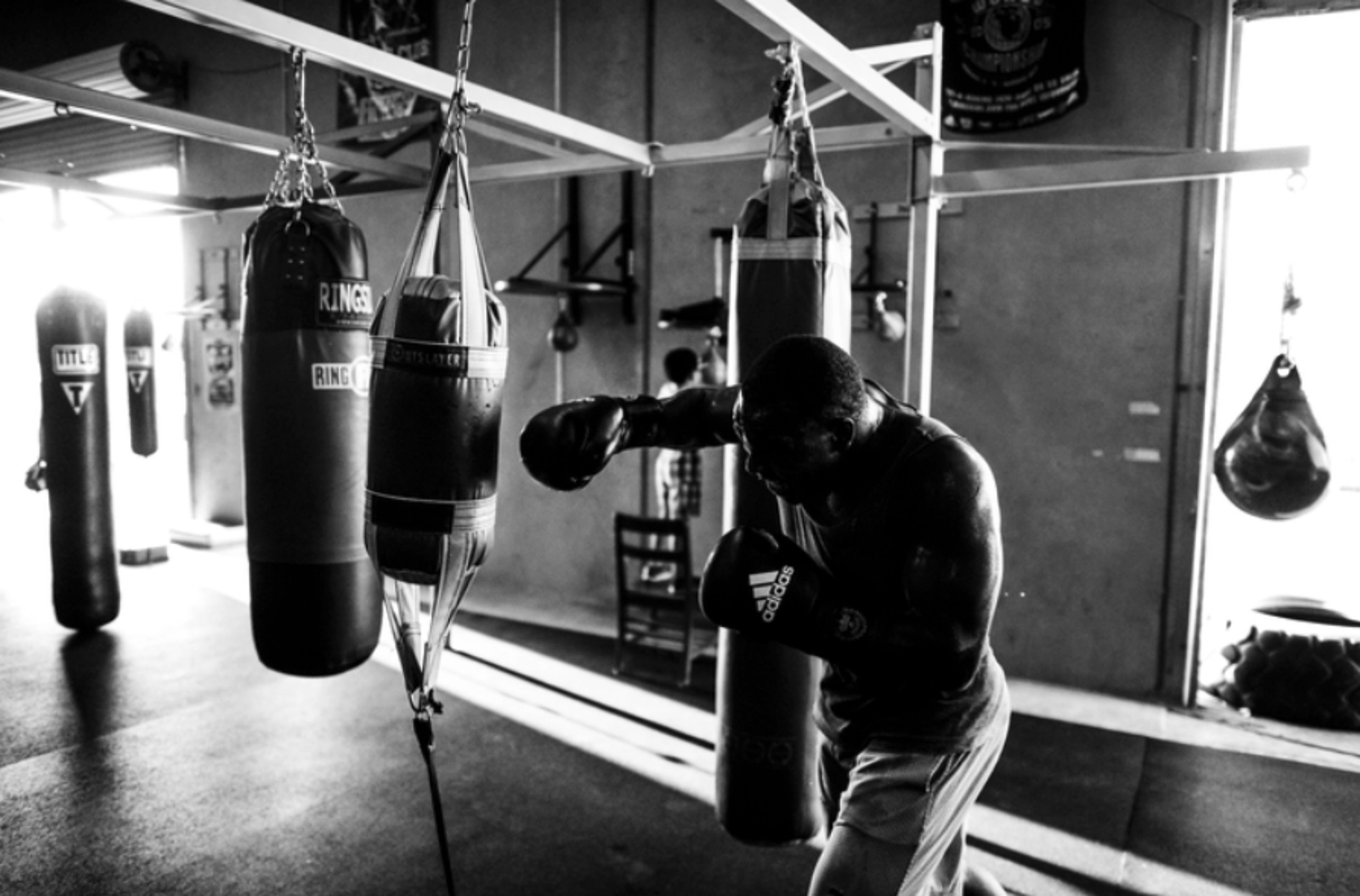 A boxer trains by throwing punches at a heavy punching bag in a dimly lit gym.