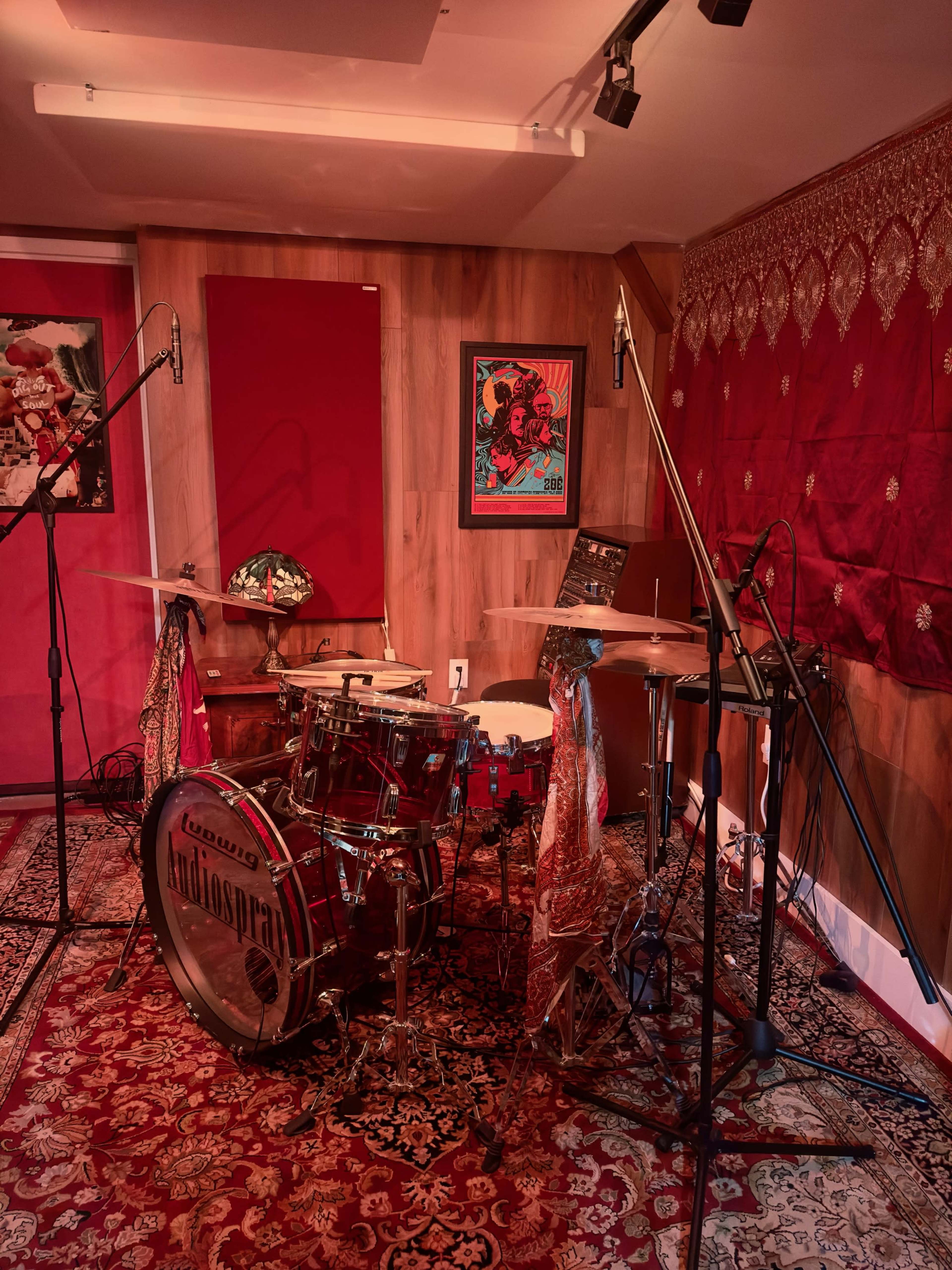 A drum set is arranged in a sound studio with red walls and decorative elements, including microphones positioned for recording.