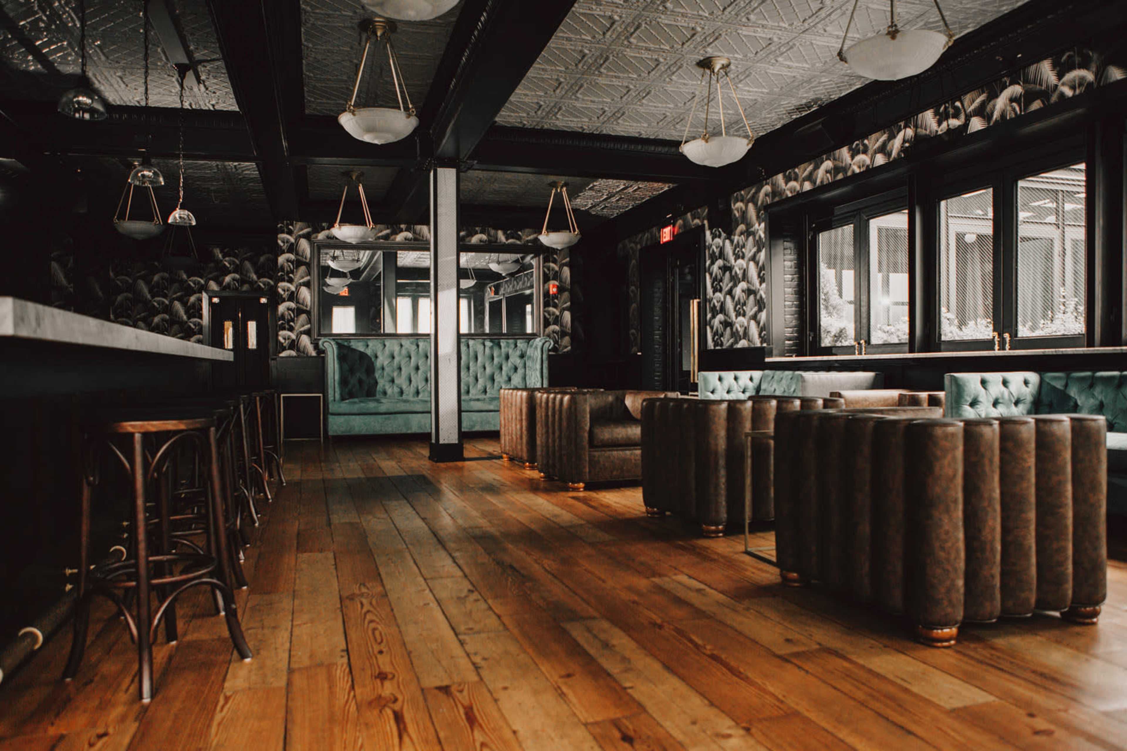 A stylish lounge with tufted seating, hardwood floors, and large windows surrounded by patterned wallpaper.