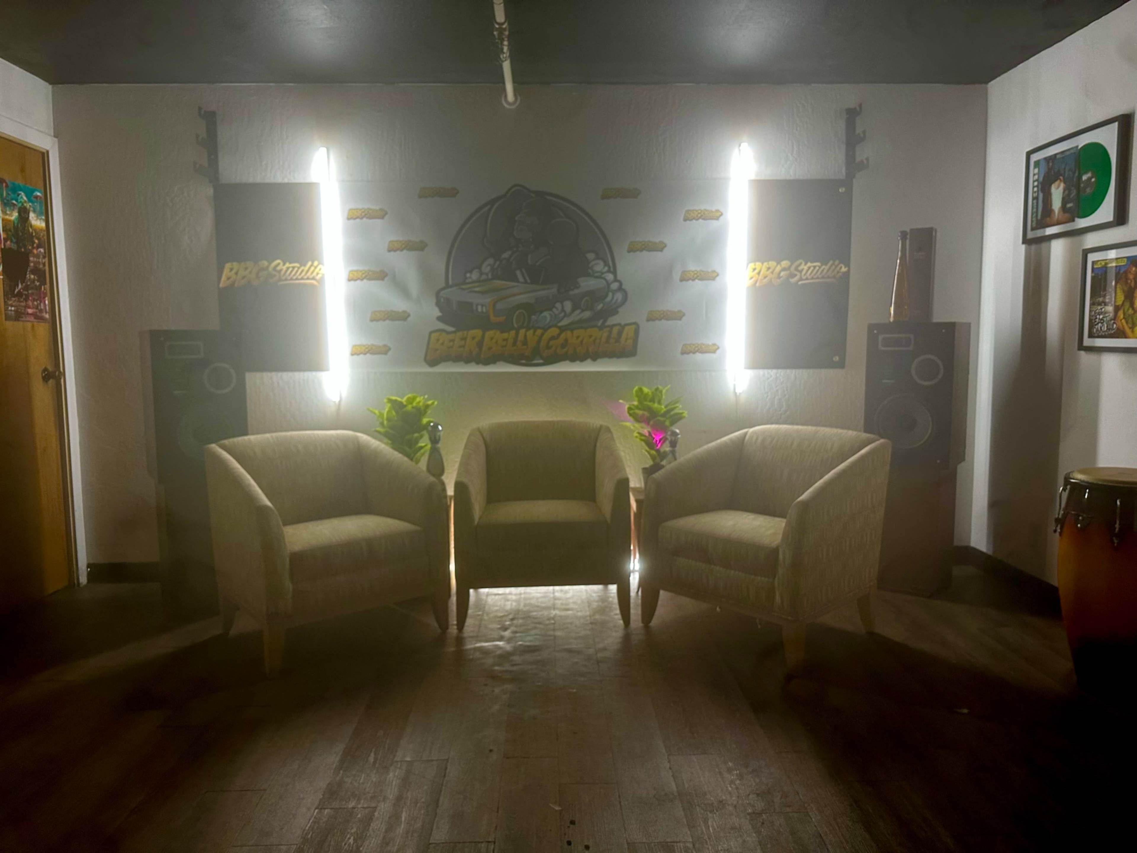 The image shows a small room with two upholstered chairs placed facing each other, illuminated by wall-mounted lights, and featuring a large mural on the wall.