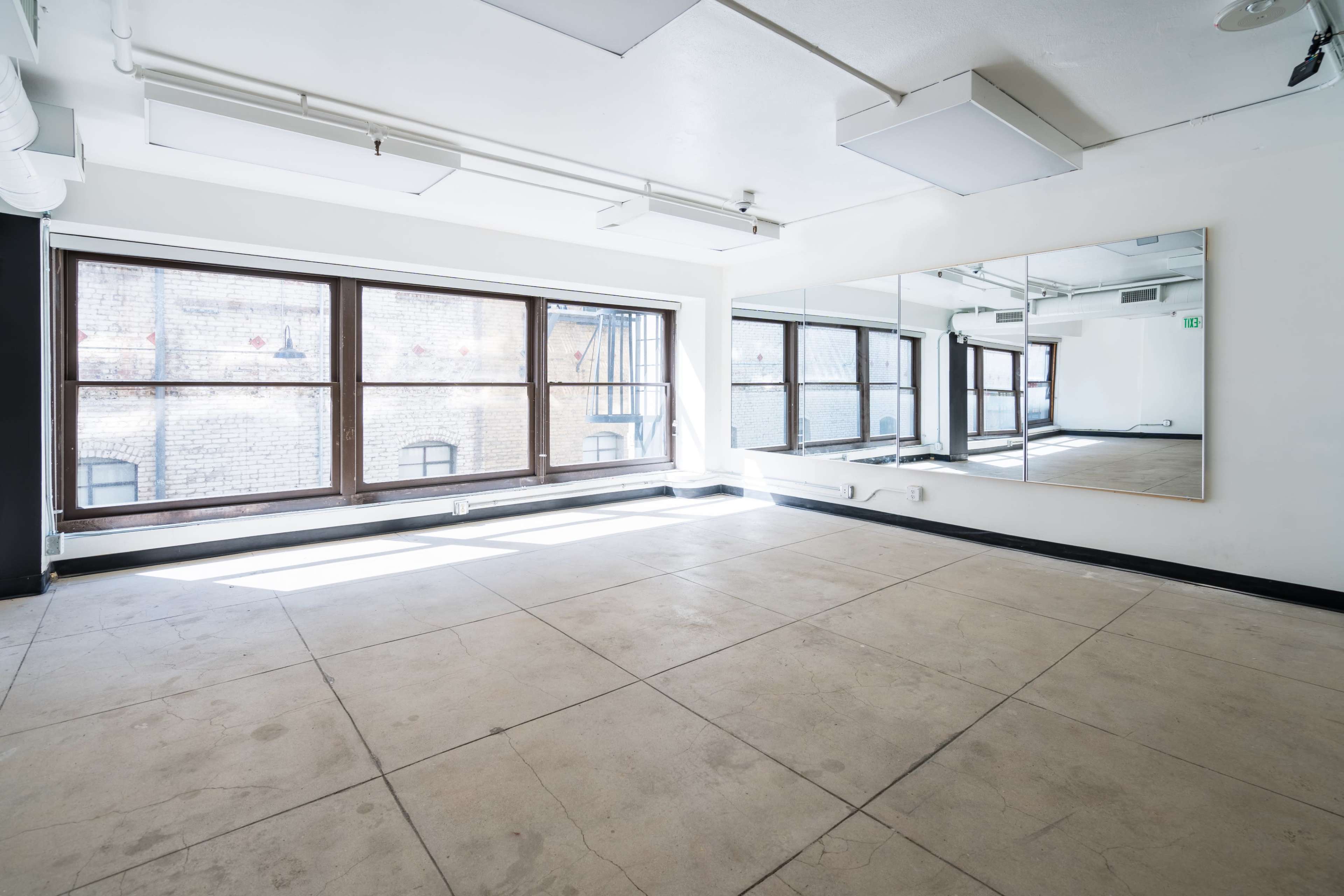 An empty room with large windows on one side and a full-length mirror on the opposite wall.