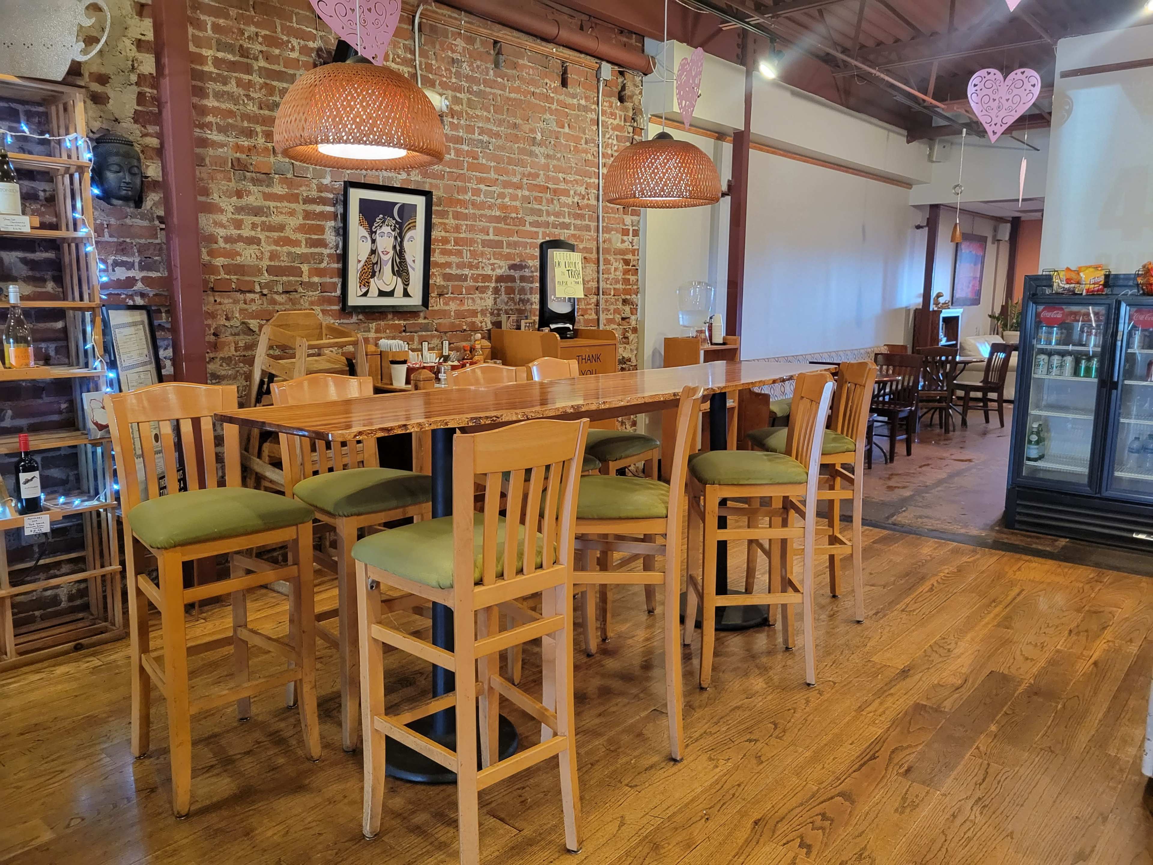 A rustic restaurant interior with wooden barstools, a long wooden table, exposed brick walls, and decorative pendant lights.