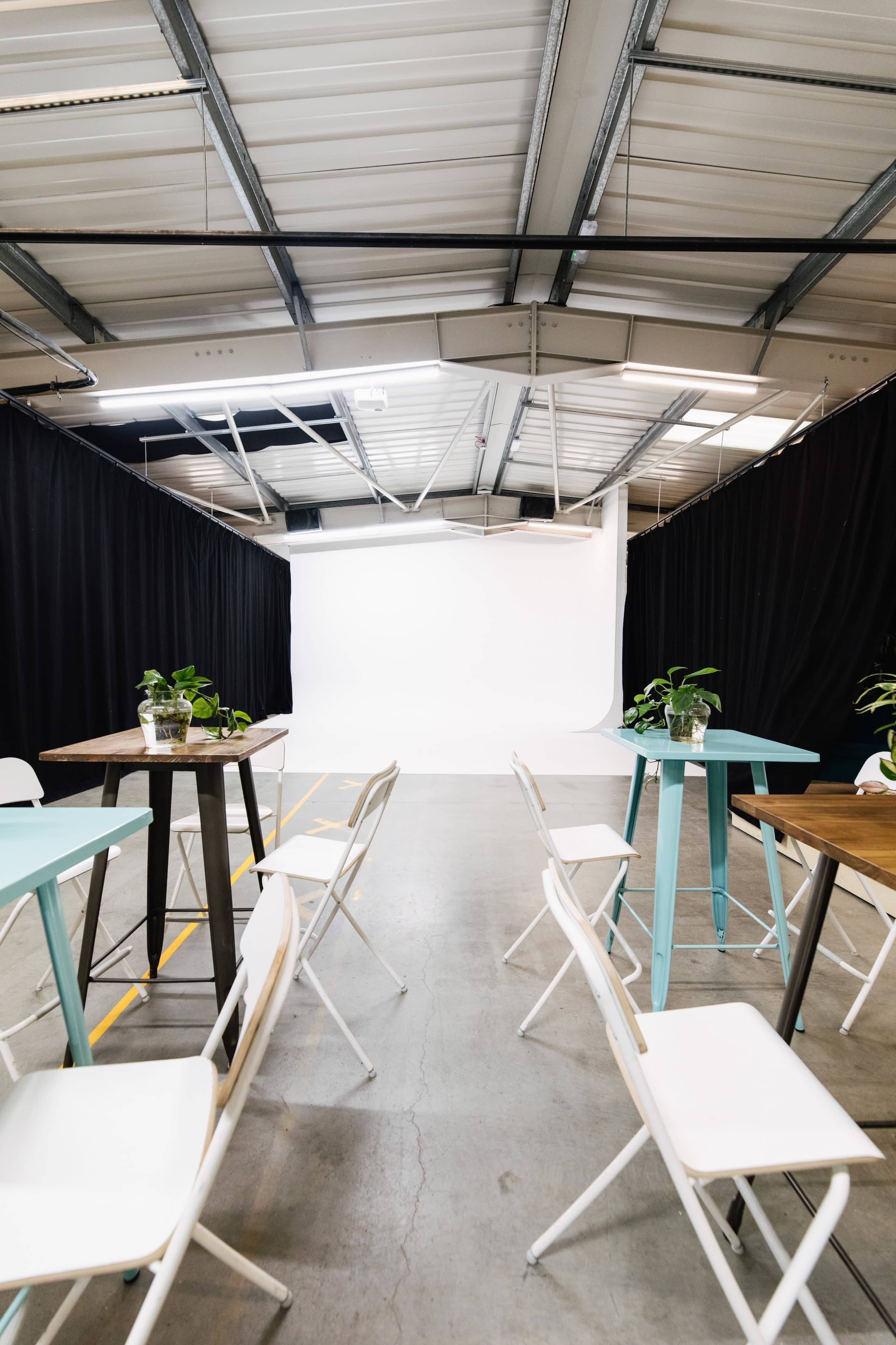 A spacious studio features several tables and chairs arranged in rows, leading to a plain white backdrop at the far end.