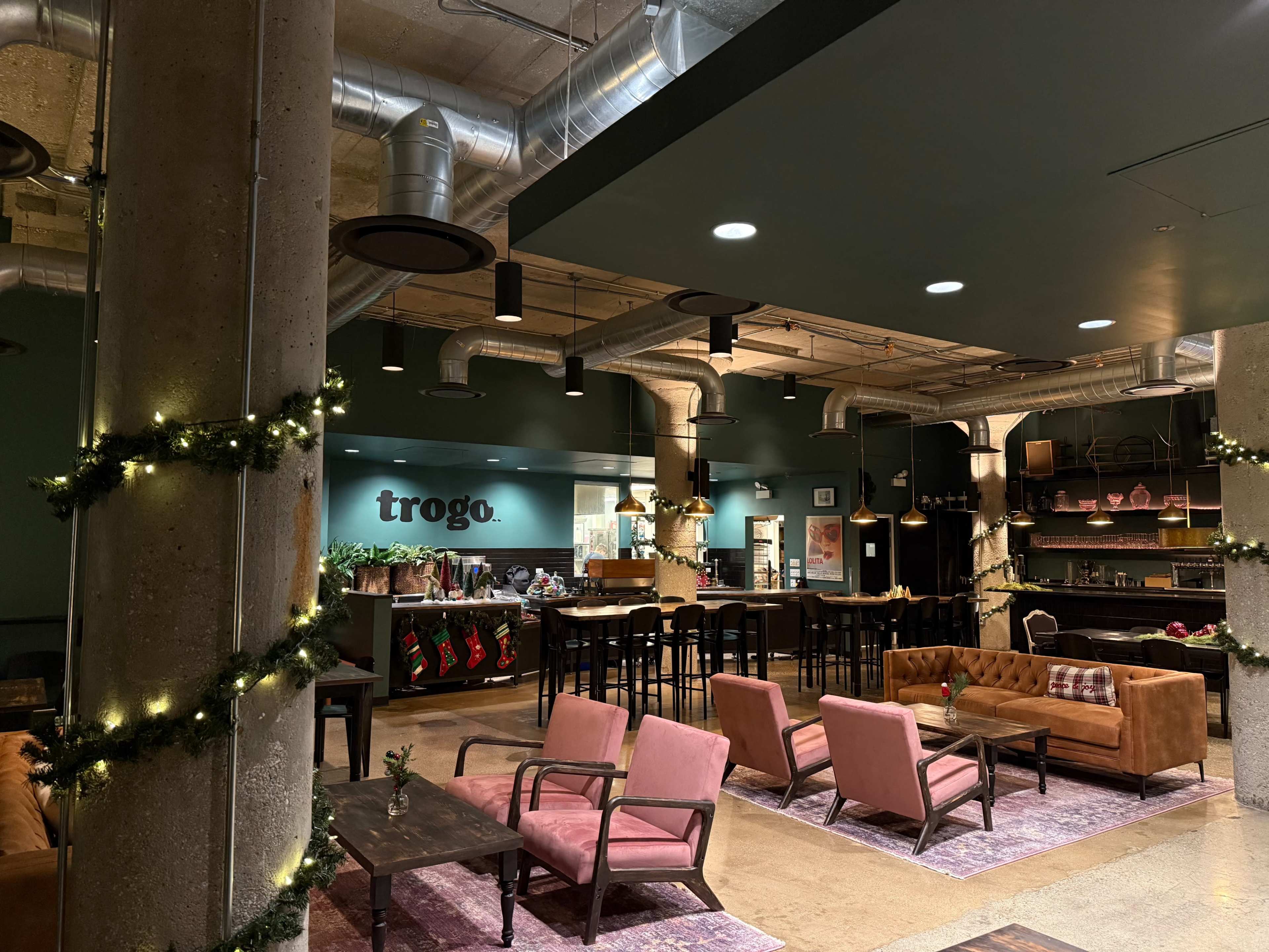 The image shows a modern café interior with cozy seating areas, a bar counter, and decorative elements including Christmas stockings and string lights.