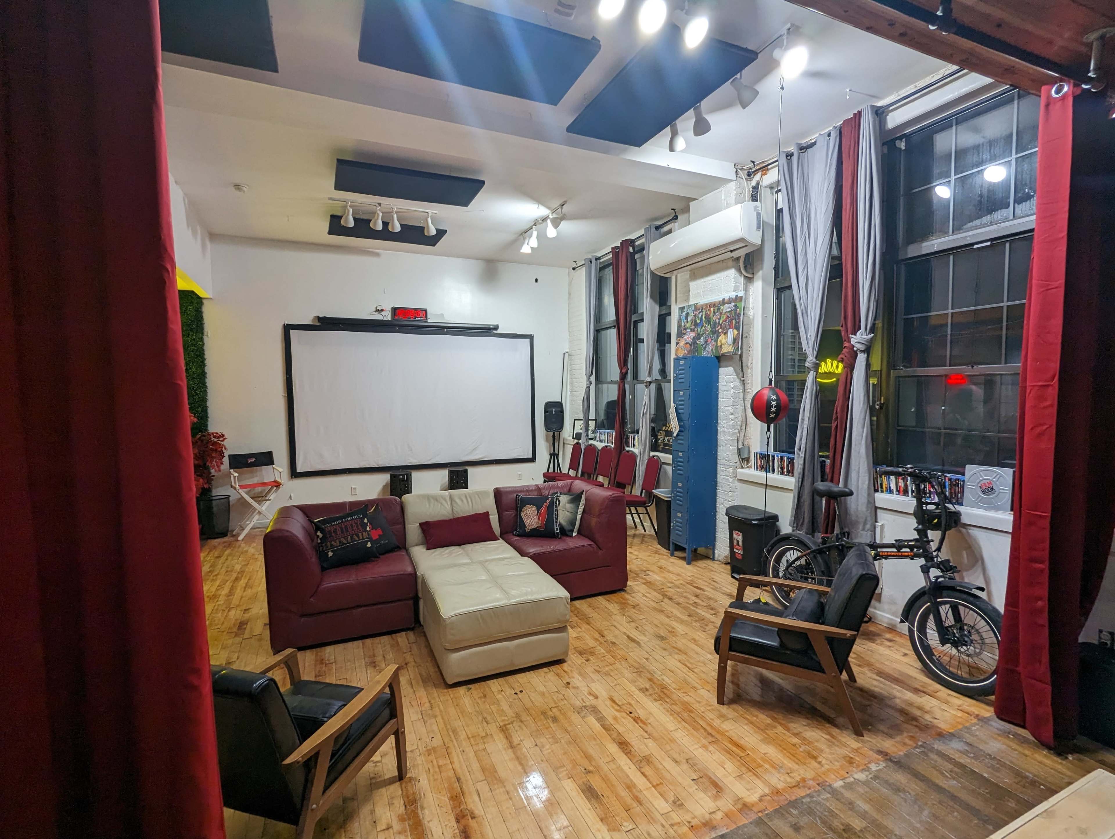 A spacious indoor area with a seating arrangement that includes a red and beige couch, chairs, a large screen, and a bicycle in the background.