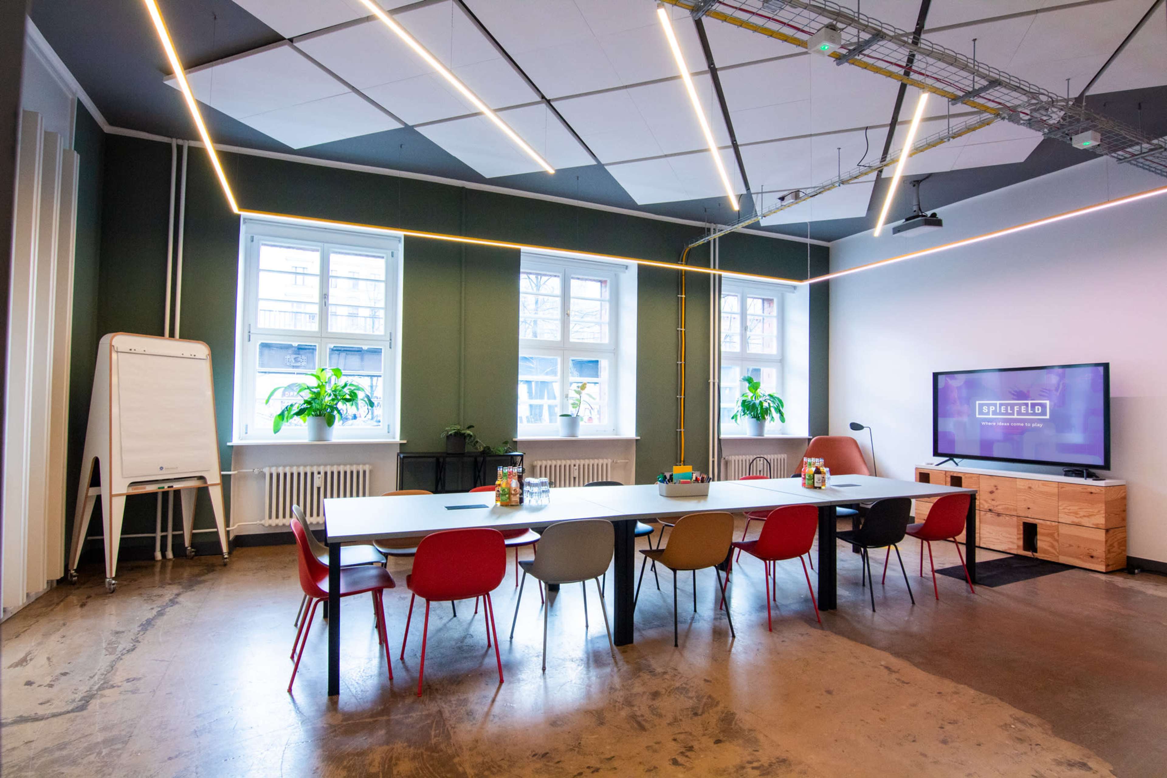 A modern conference room with a long table, colorful chairs, a whiteboard, and a TV mounted on the wall.
