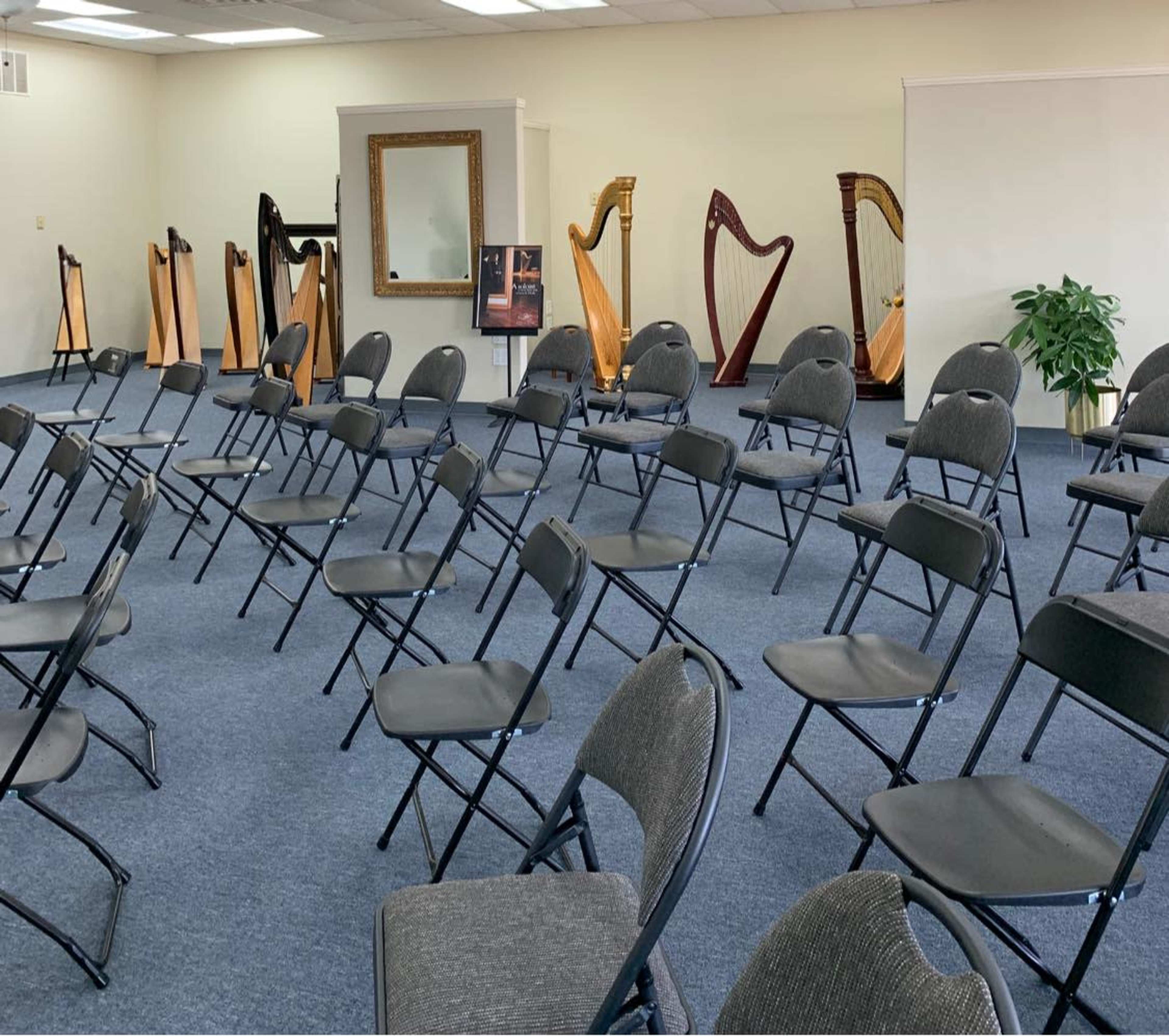 The image shows a room filled with folding chairs arranged in rows, facing several wooden harps displayed in the background.