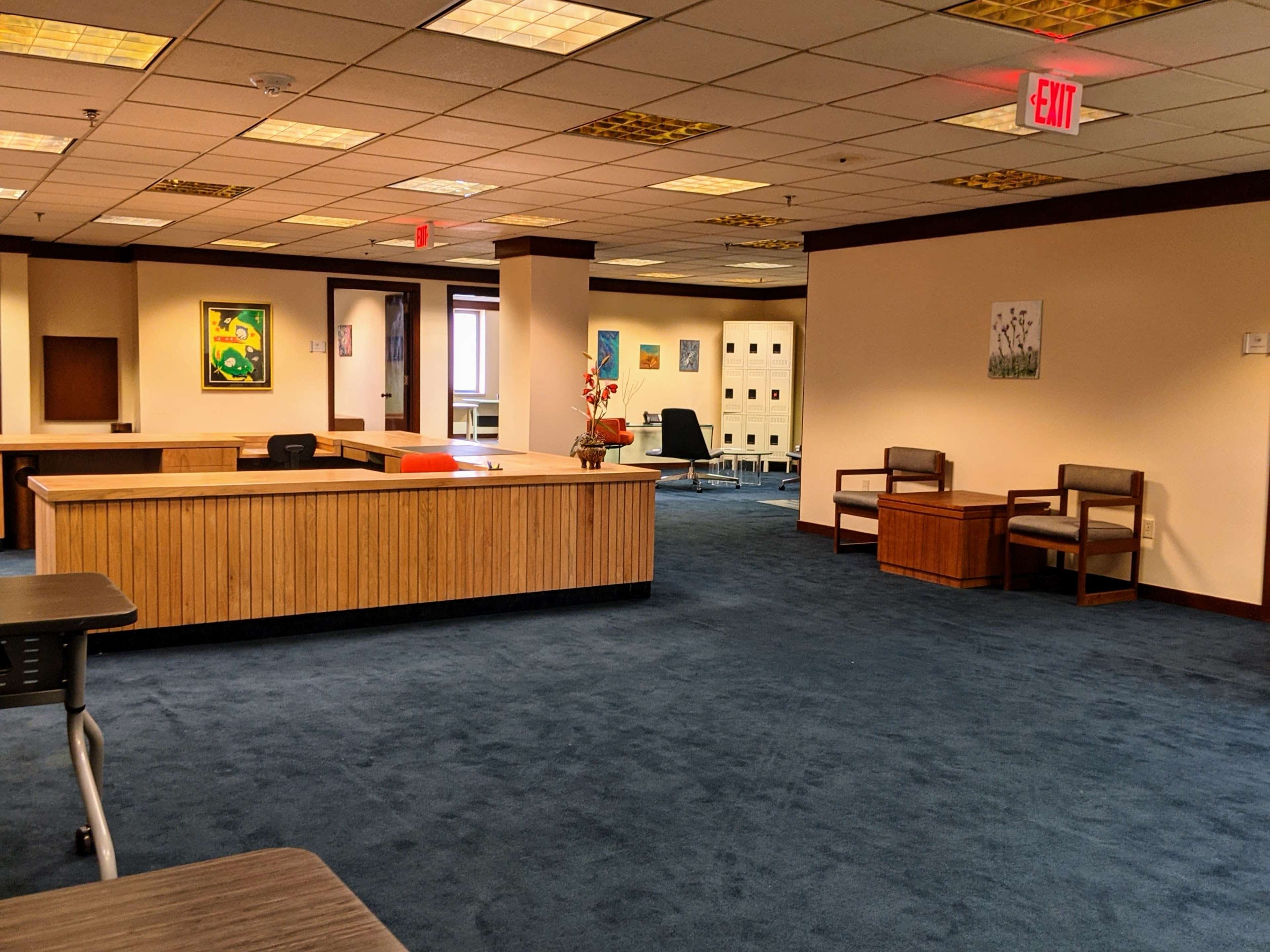 A spacious office area with blue carpeting, wooden reception desks, and various paintings on the walls.
