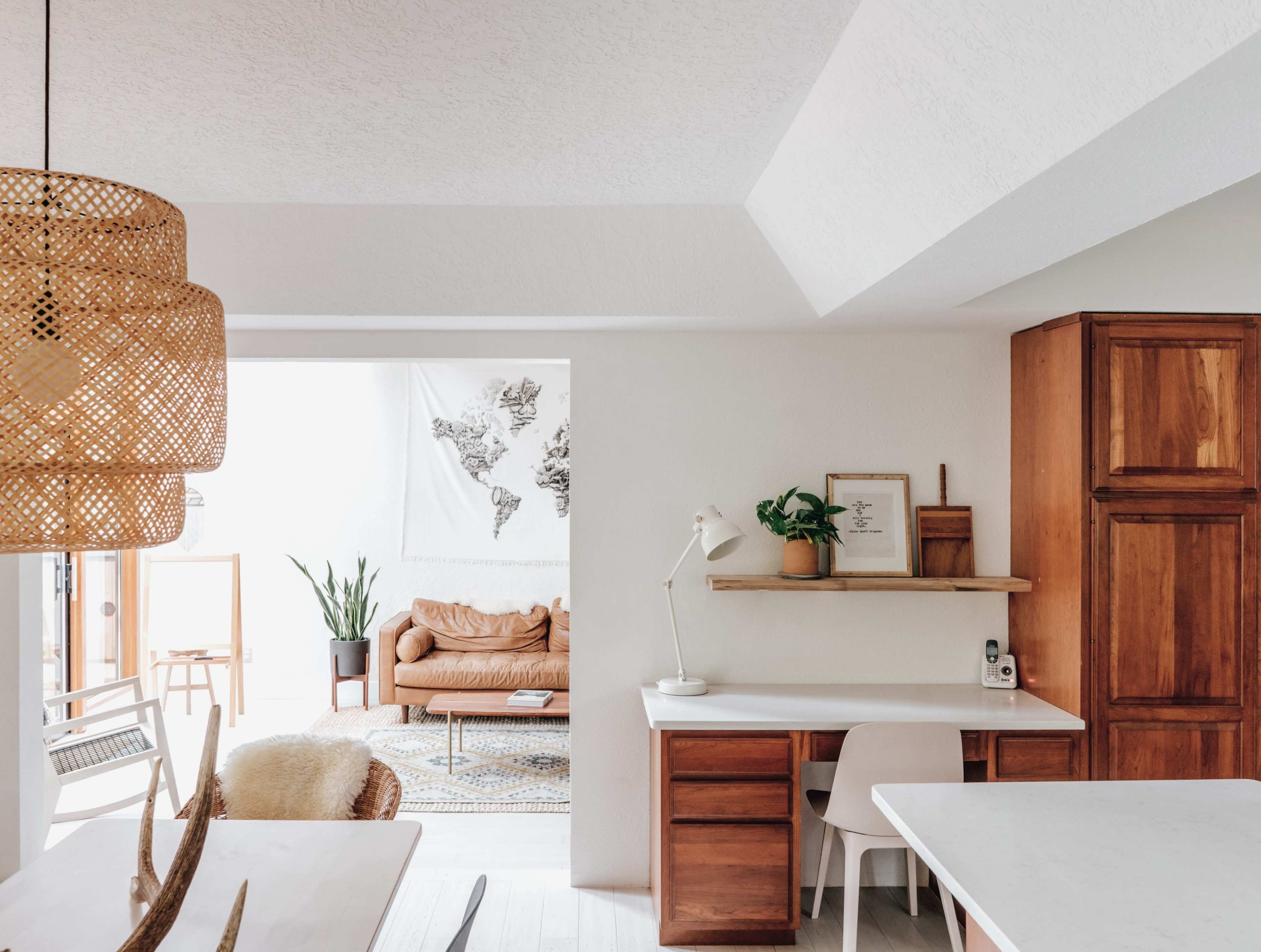 A modern, open kitchen and living area with wooden cabinetry, a hanging light fixture, and a couch in a bright, neutral-toned space.