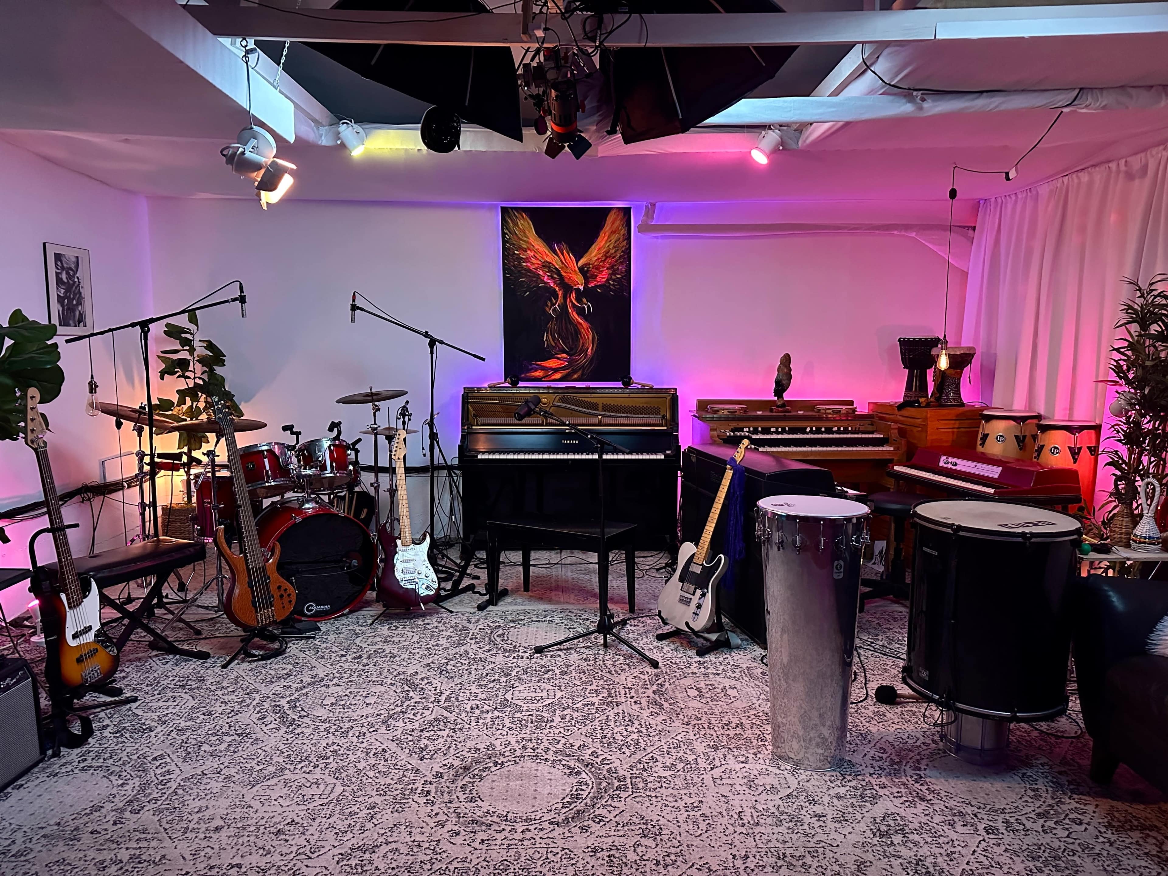 The image shows a music studio filled with various musical instruments, including guitars, drums, a grand piano, and percussion instruments, all set against a brightly lit backdrop with colorful lighting.