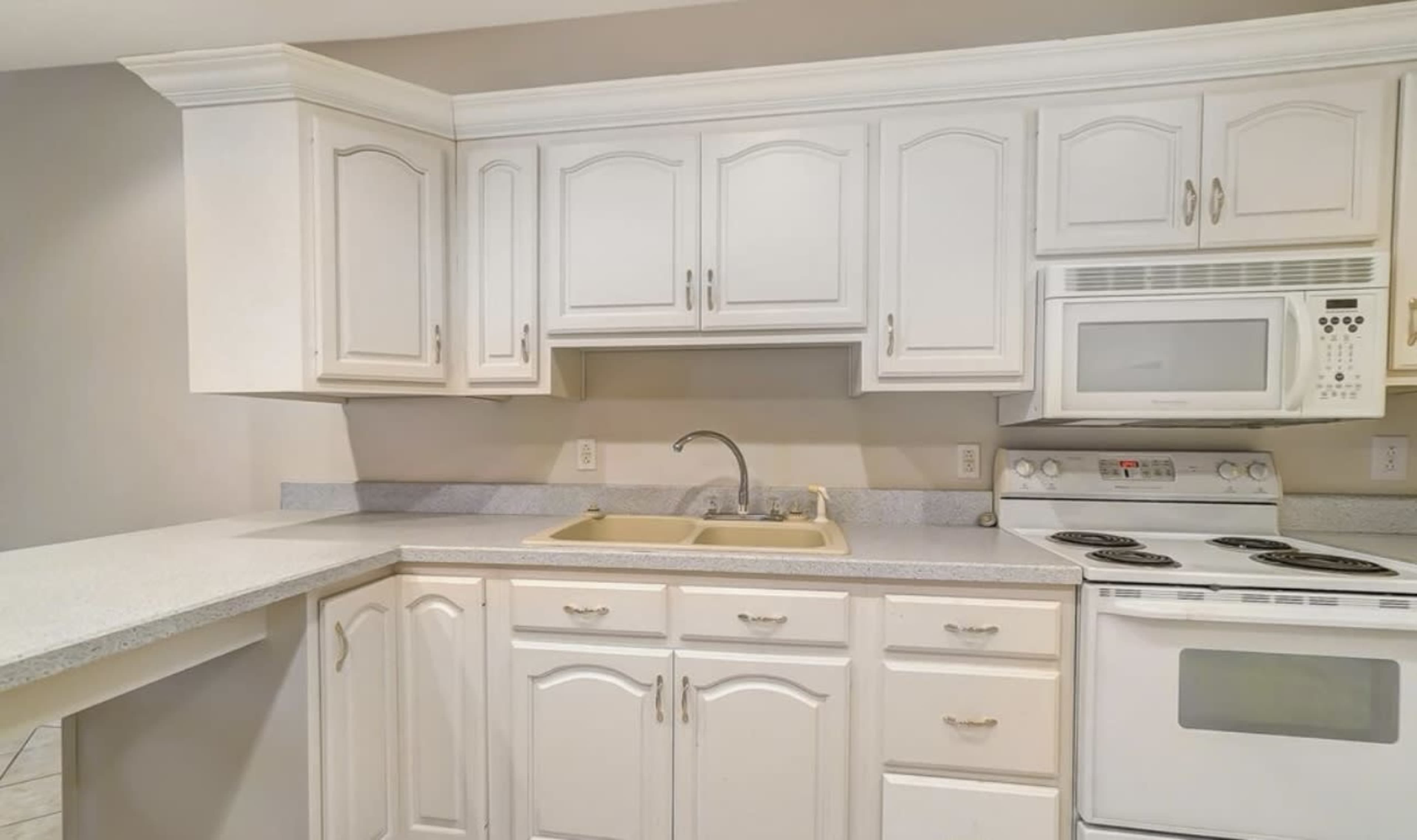 The image shows a kitchen with white cabinetry, a double sink, a microwave, and a stove with an oven.
