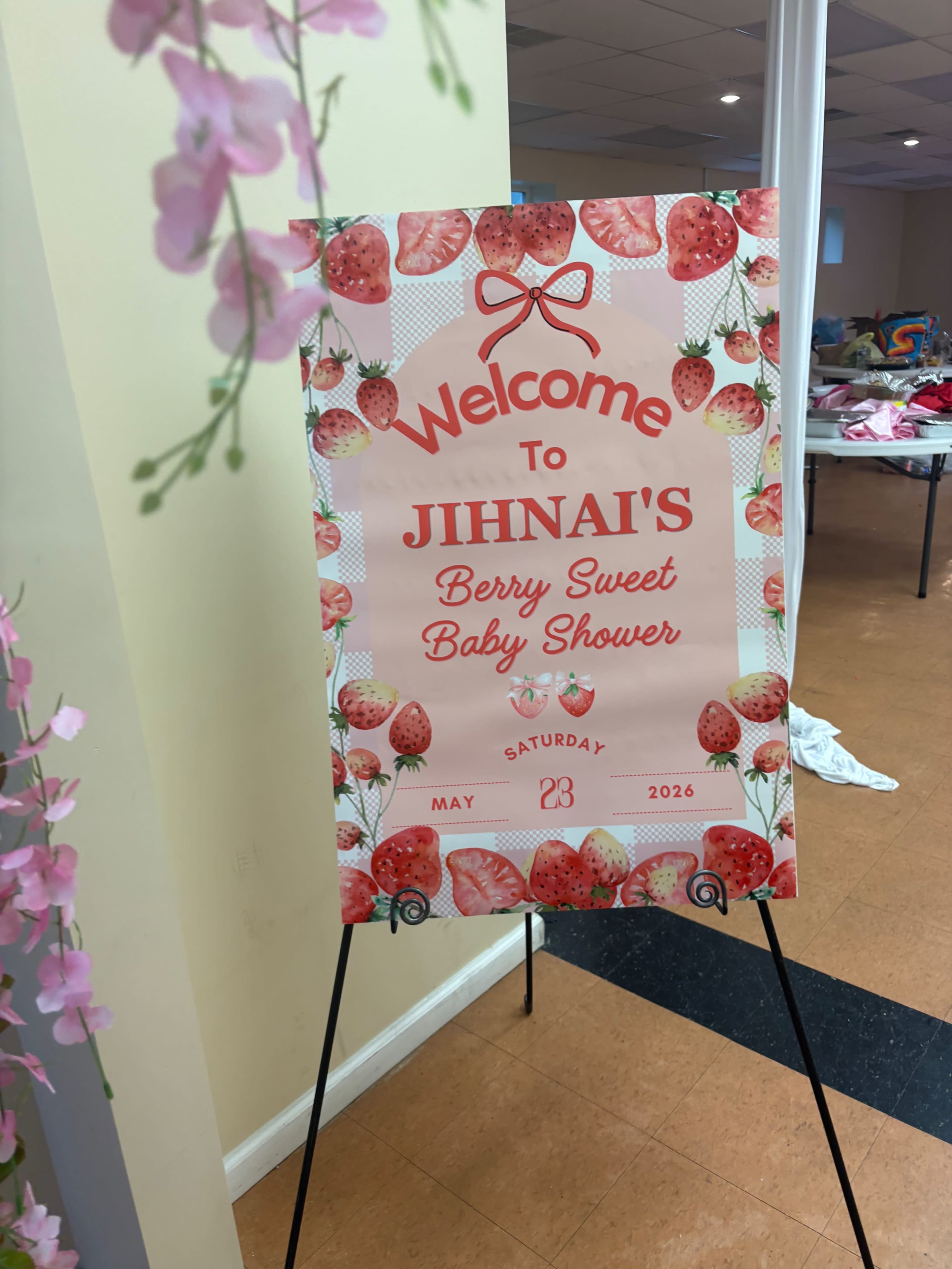 A decorative sign welcomes guests to Jihnai's berry-themed baby shower, featuring strawberries and colorful text, displayed on an easel.