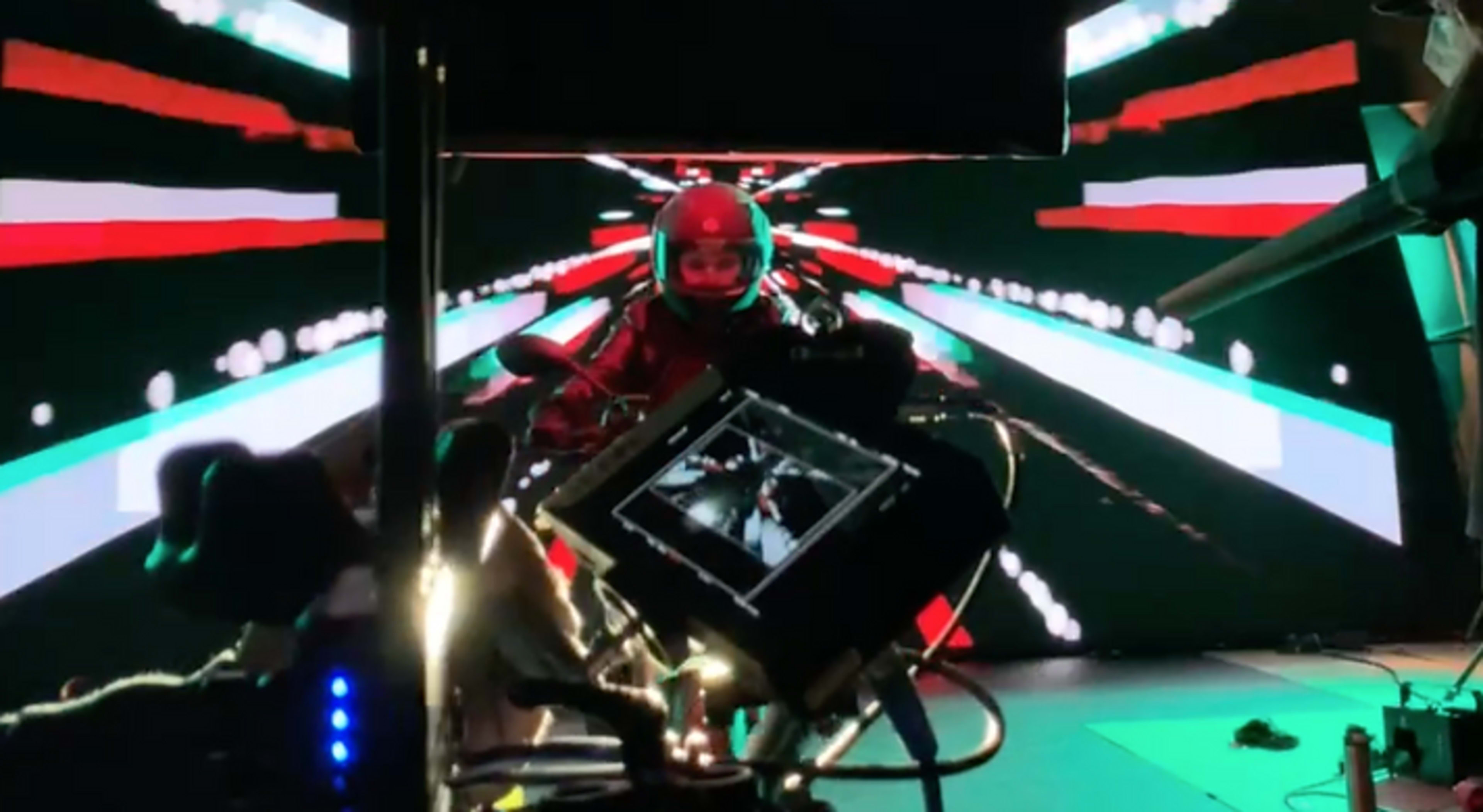 A motorcyclist is positioned in front of a vibrant, digitally animated backdrop featuring red, green, and white lines.