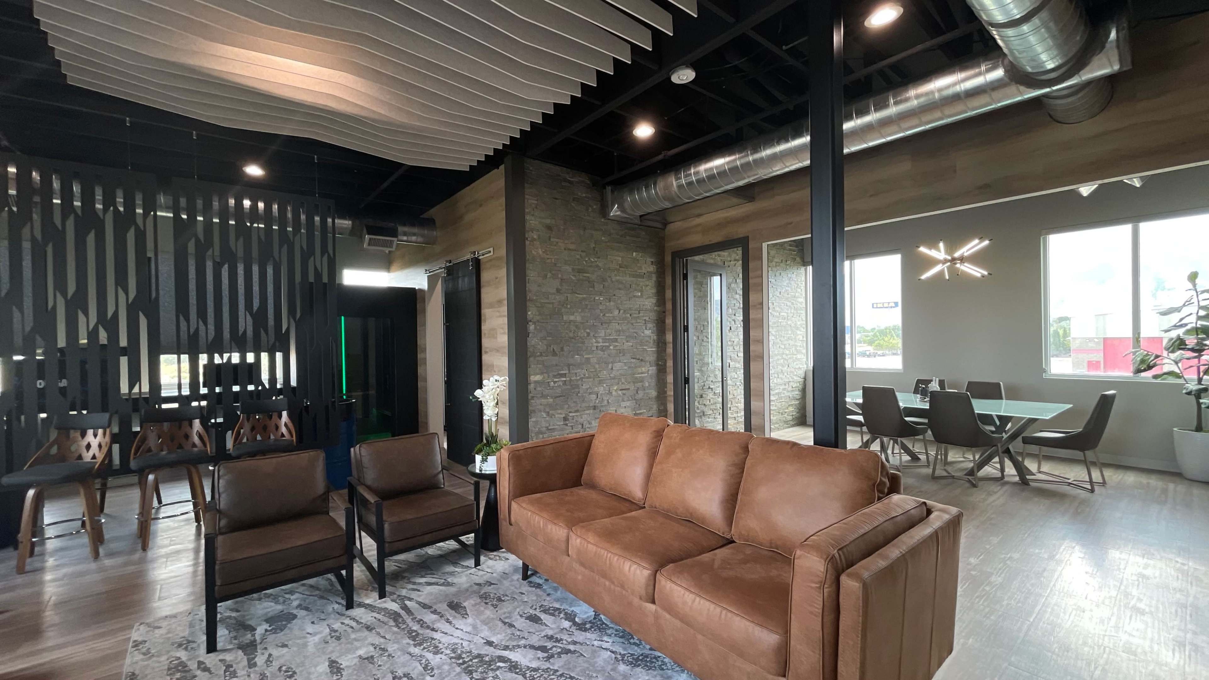 A modern lounge area featuring a brown sofa, two chairs, a dining table, and large windows with natural light.