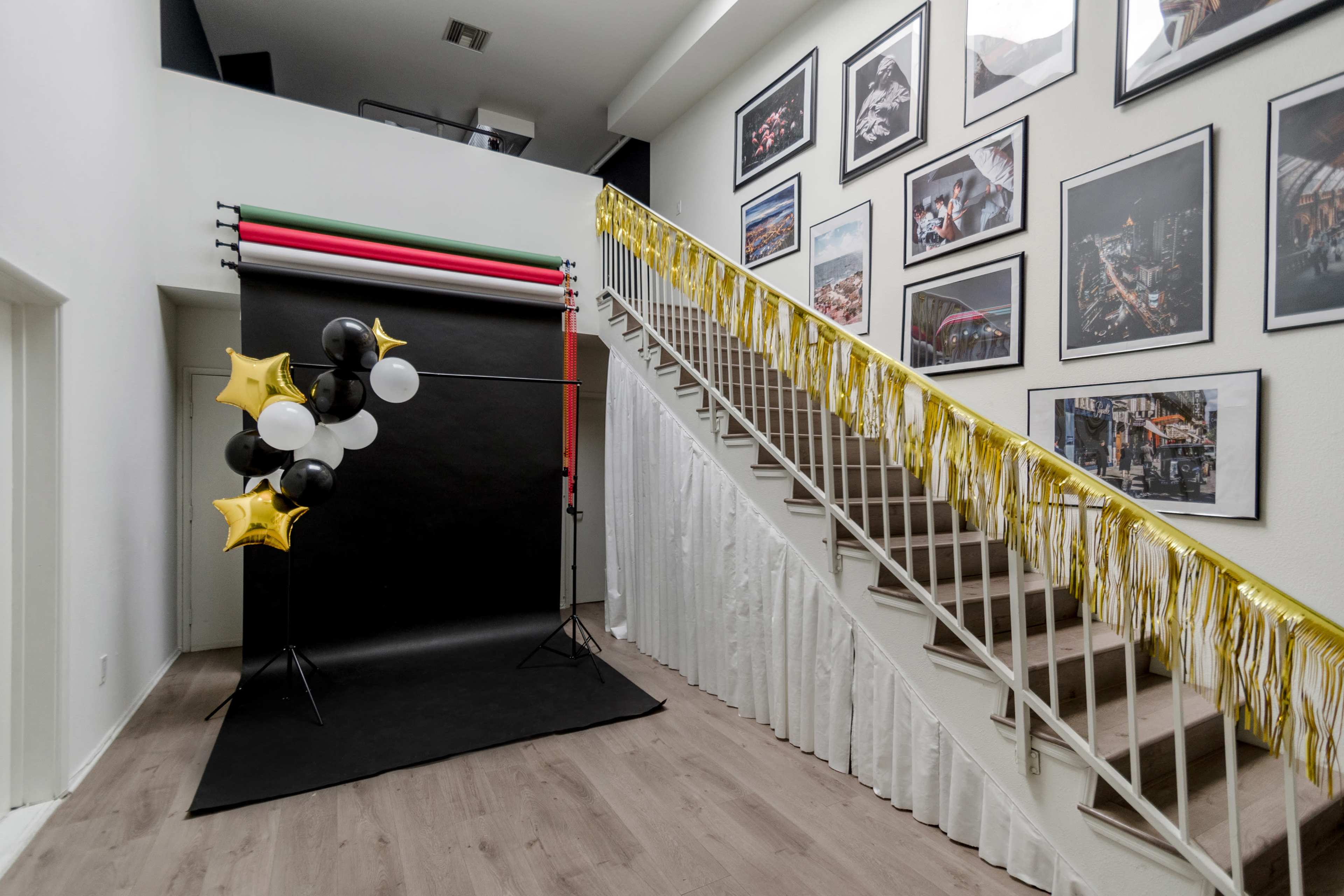 The image shows a decorated staircase with a black backdrop and balloons on one side, alongside framed photographs on the wall.